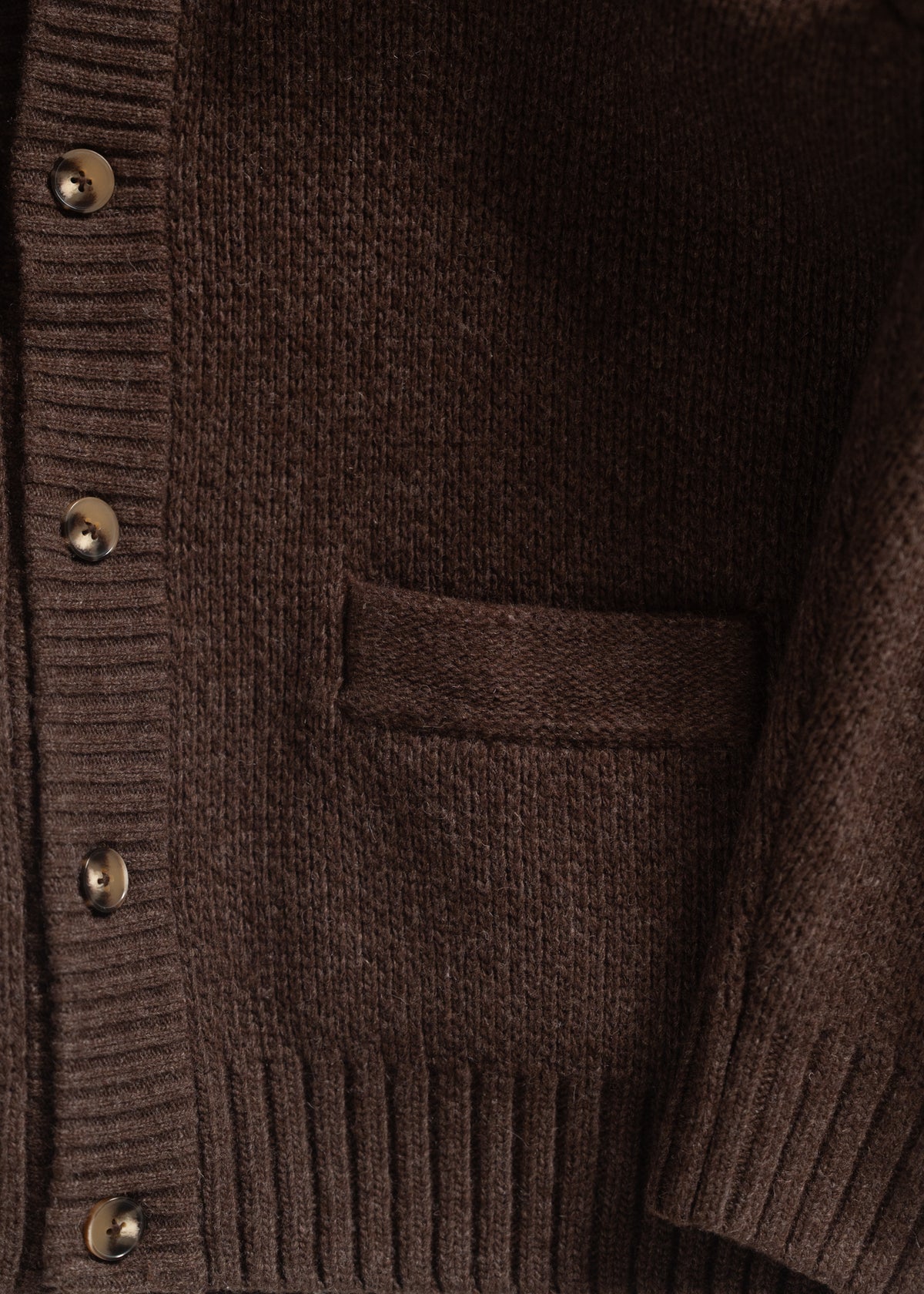 Close-up of a brown knit cardigan with ribbed cuffs, button details, and a pocket, showcasing its texture and design elements.