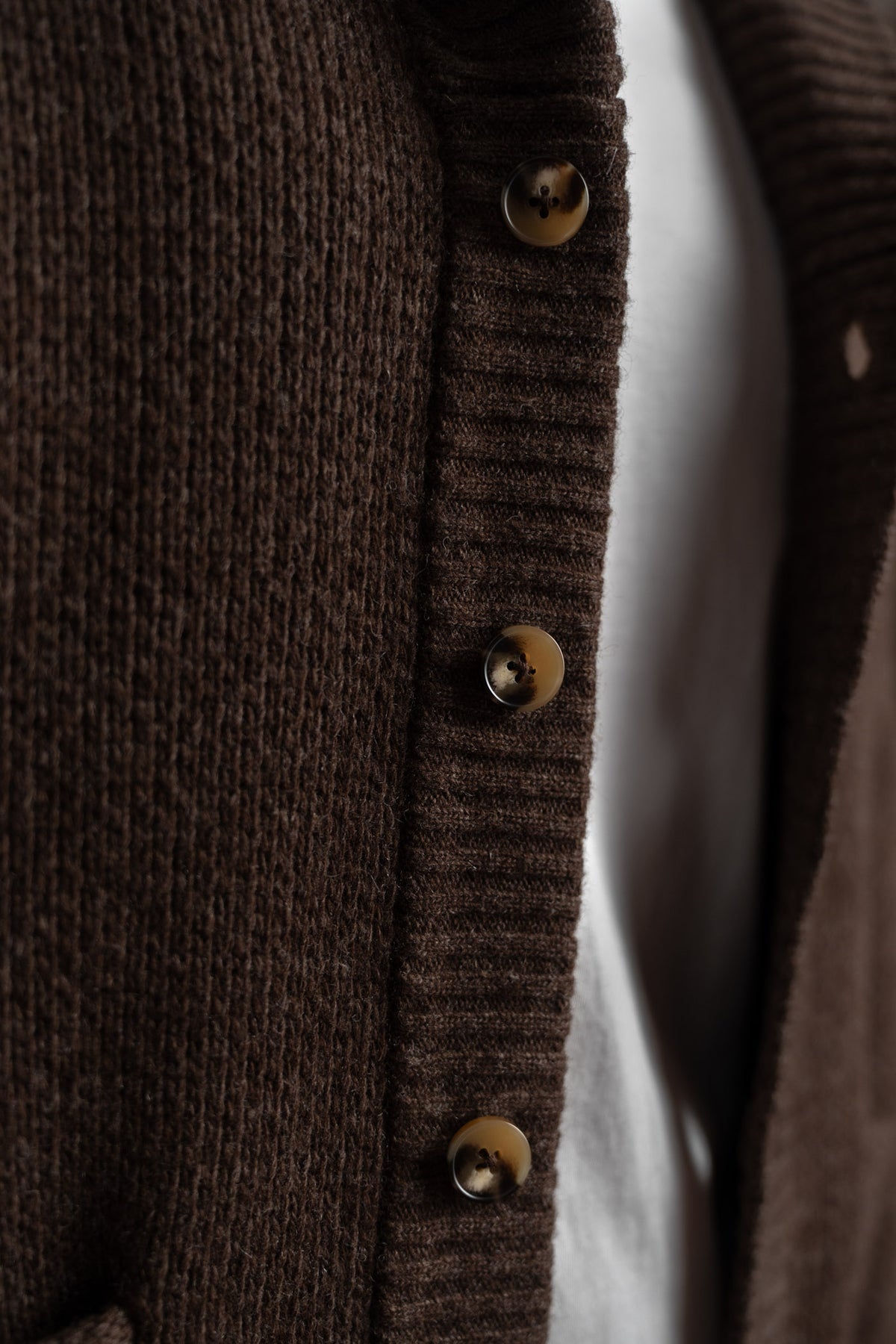 Close-up of a brown knit cardigan with four buttons over a white shirt, highlighting texture and detail.