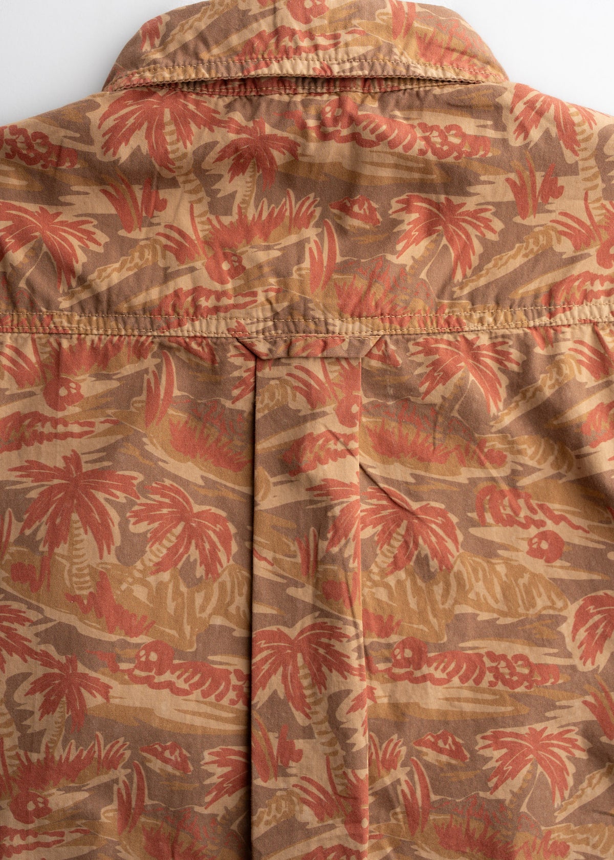 Close-up of a brown shirt with a red palm tree pattern, showcasing the back yoke and pleat detail.