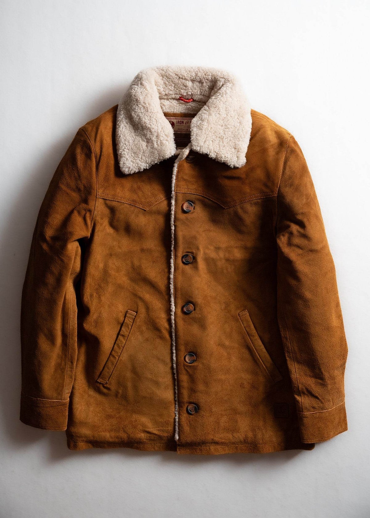 Brown suede jacket with a white shearling collar, buttoned front, and side pockets, displayed on a plain white background.