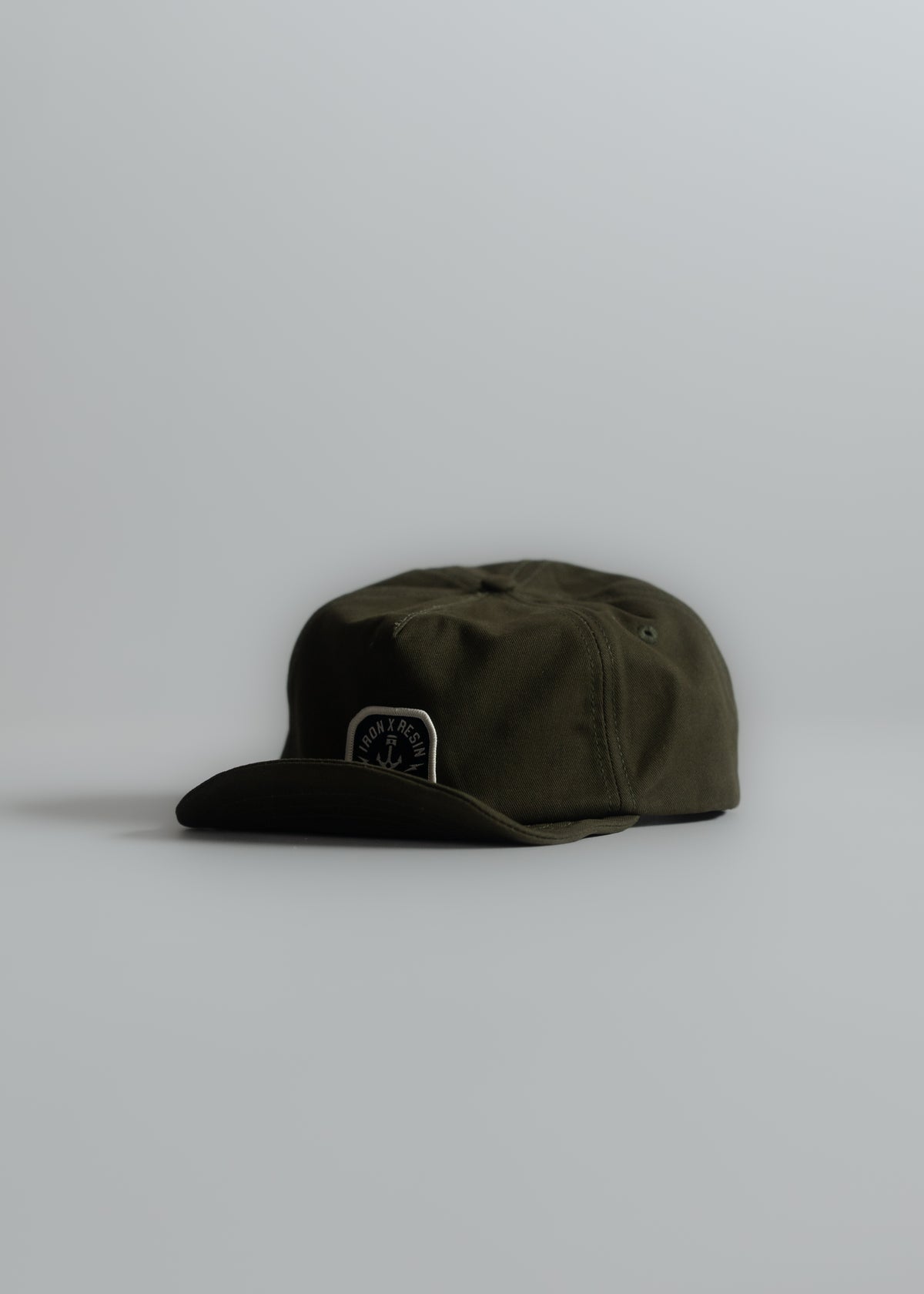 Olive green cap with a black brim and logo on the front, set against a plain gray background, showcasing minimalist style.