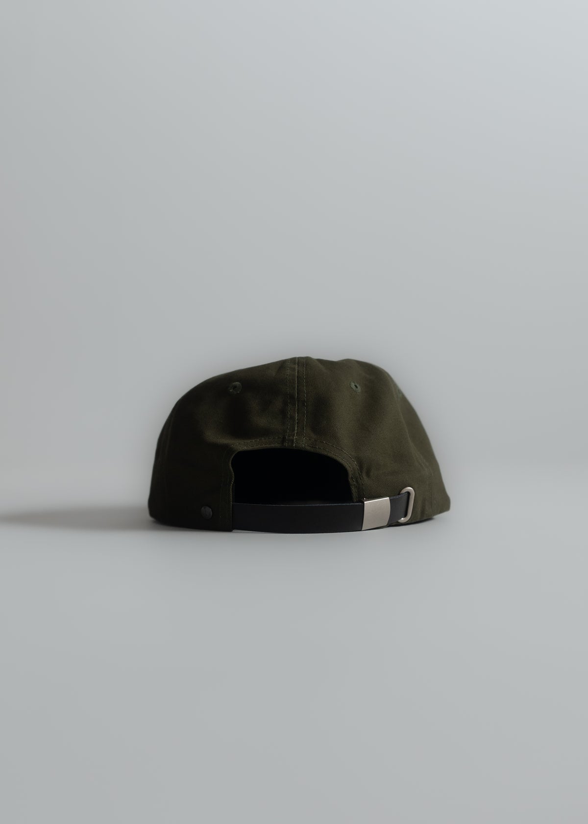A dark green baseball cap with an adjustable strap and metal buckle is placed on a light gray surface, viewed from the back.