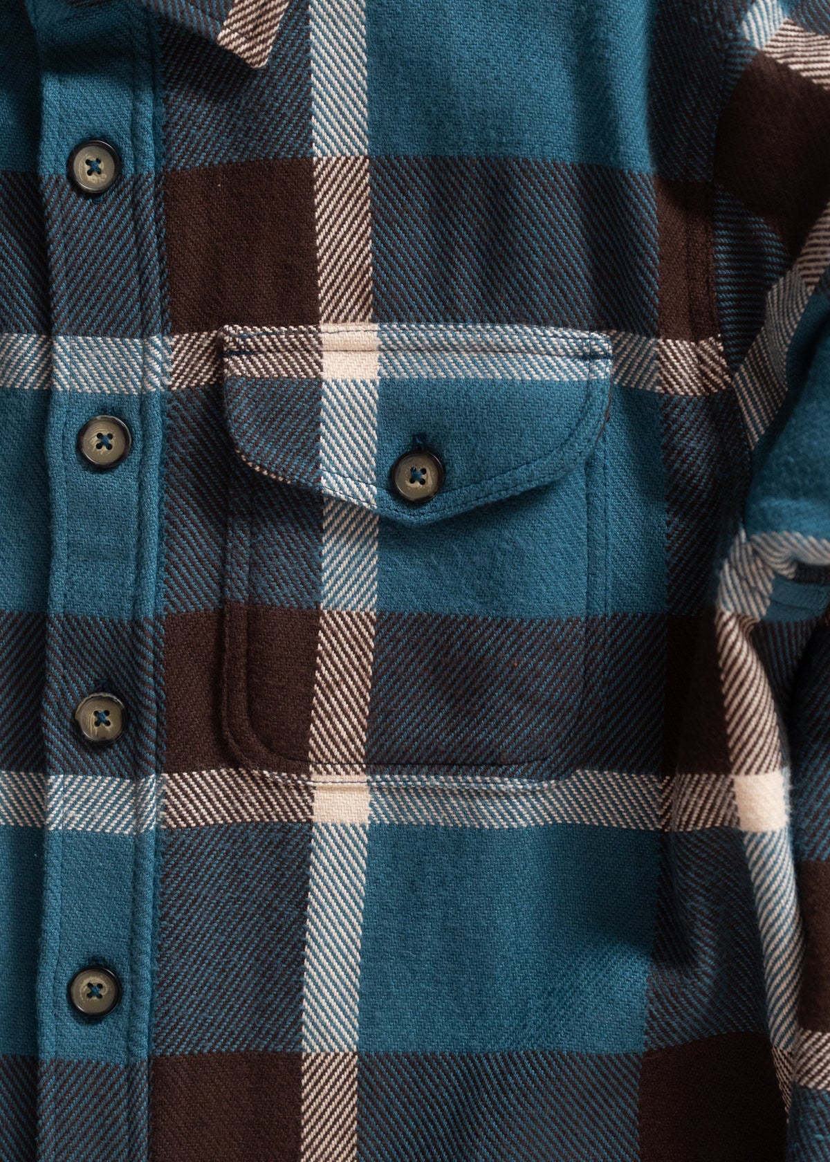 Close-up of a blue, brown, and white plaid flannel shirt with a pocket and buttons, showcasing its textured fabric.
