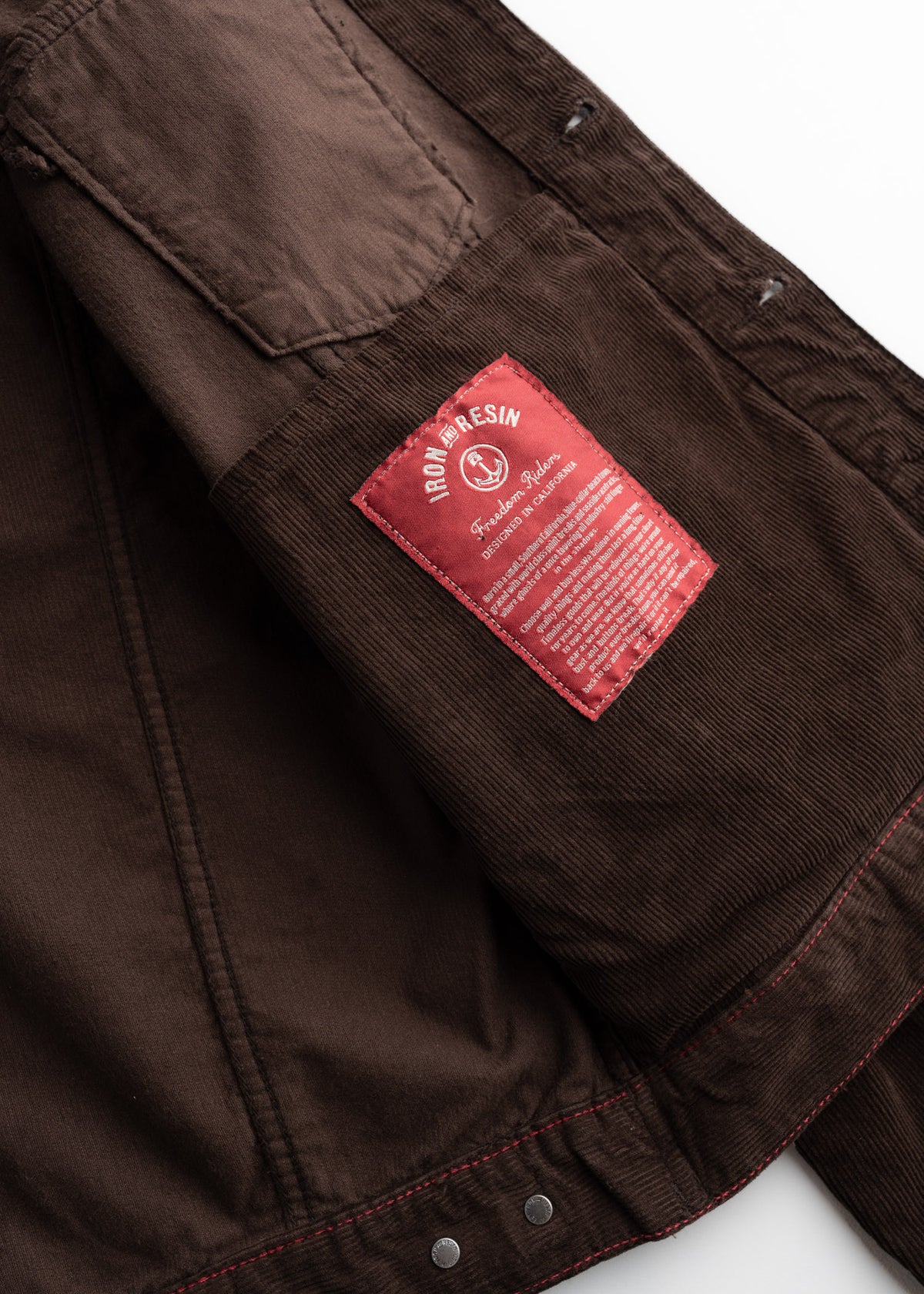 Brown jacket interior showing a red Iron and Resin label with text, highlighting the brand's craftsmanship and design details.