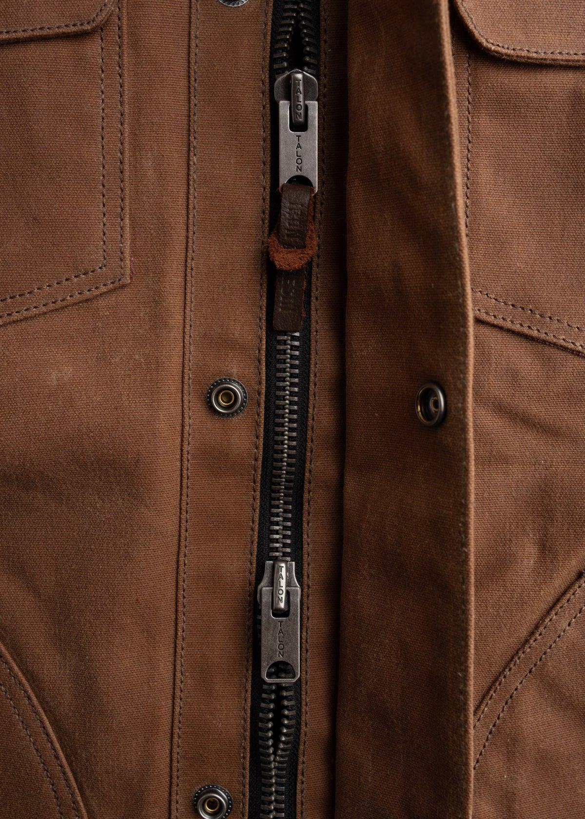 Close-up of a brown jacket with a prominent Talon zipper, showcasing detailed stitching and metal buttons on the fabric.