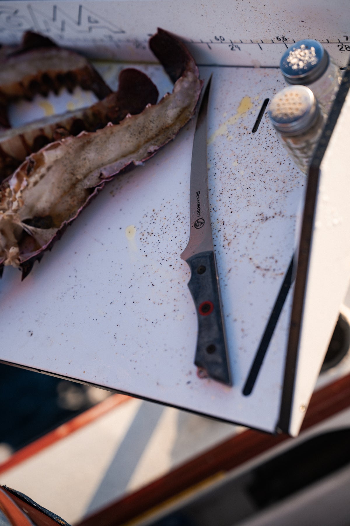 Knife on a cutting board with lobster shell and seasoning jars, ready for seafood preparation.