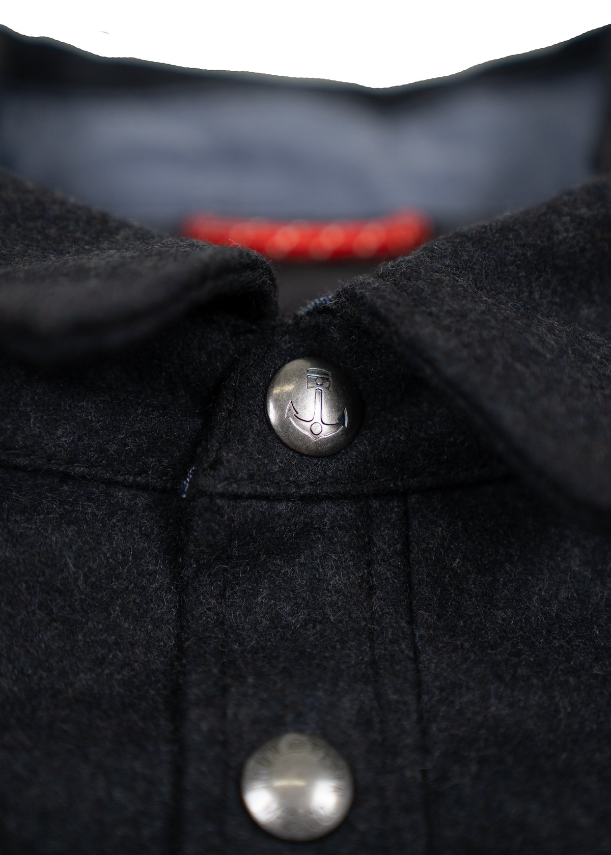 Close-up of a dark wool jacket collar with a metal button featuring an anchor design, highlighting texture and detail.