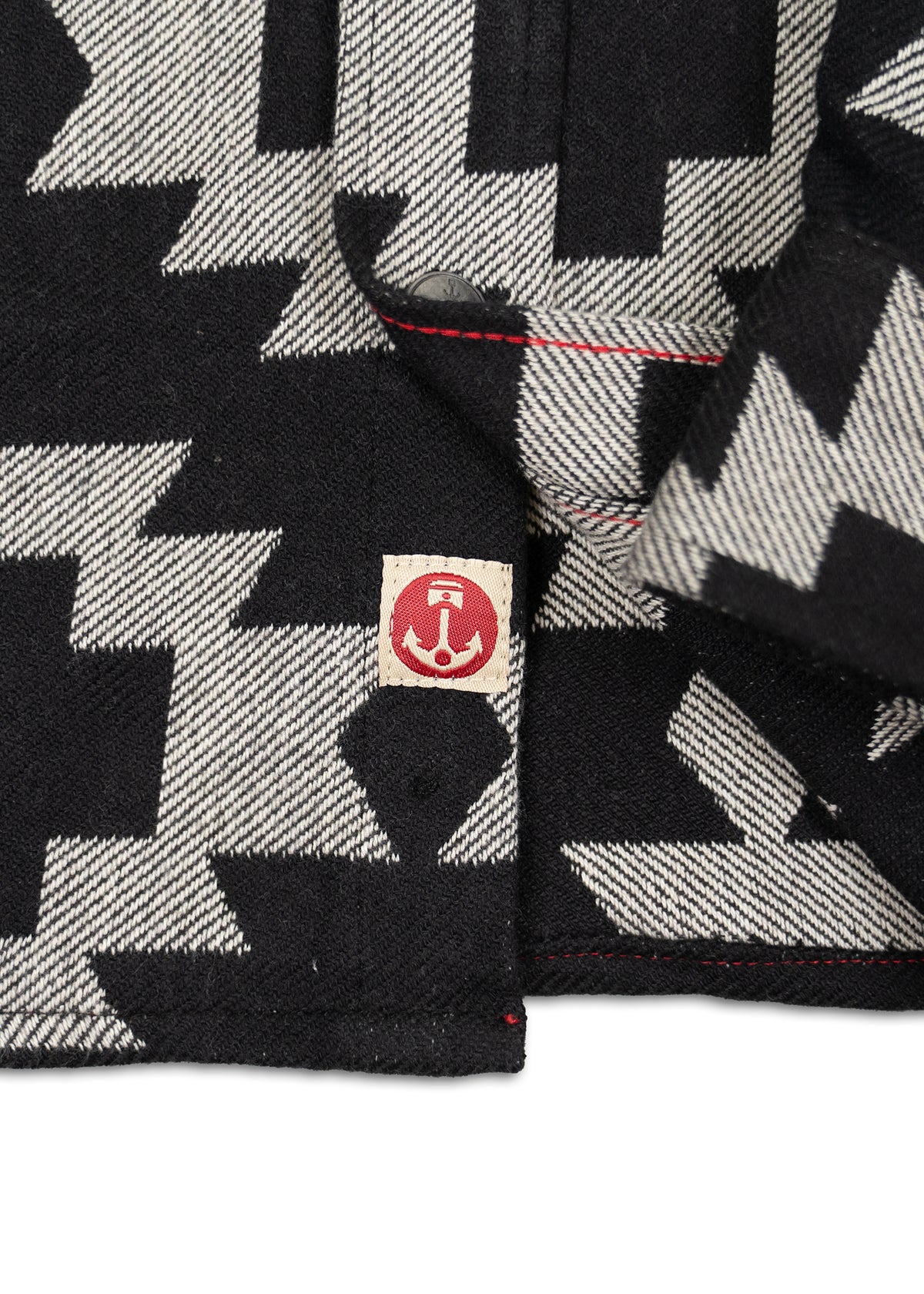 Black and white zigzag patterned fabric with a red anchor logo tag and visible red stitching detail on the edge.