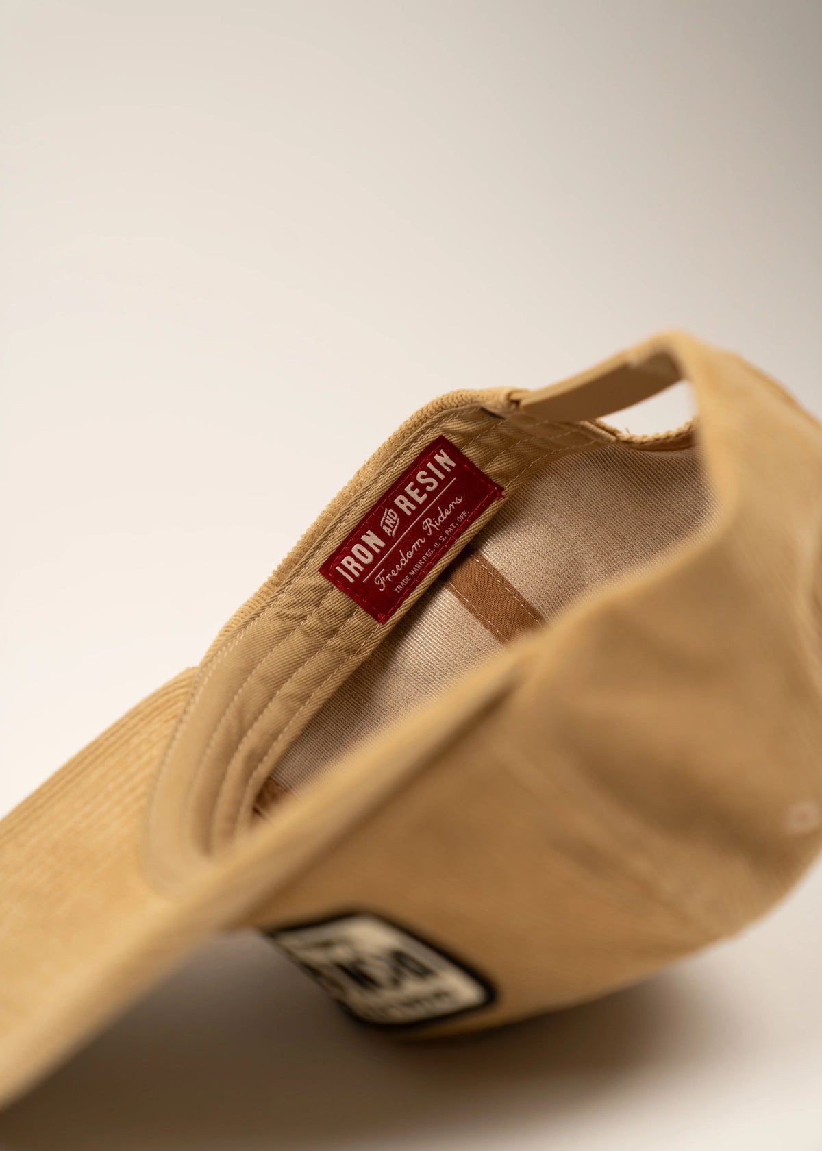 Tan cap with "Iron and Resin" label inside, showcasing craftsmanship. The exterior features a black and white patch for style.