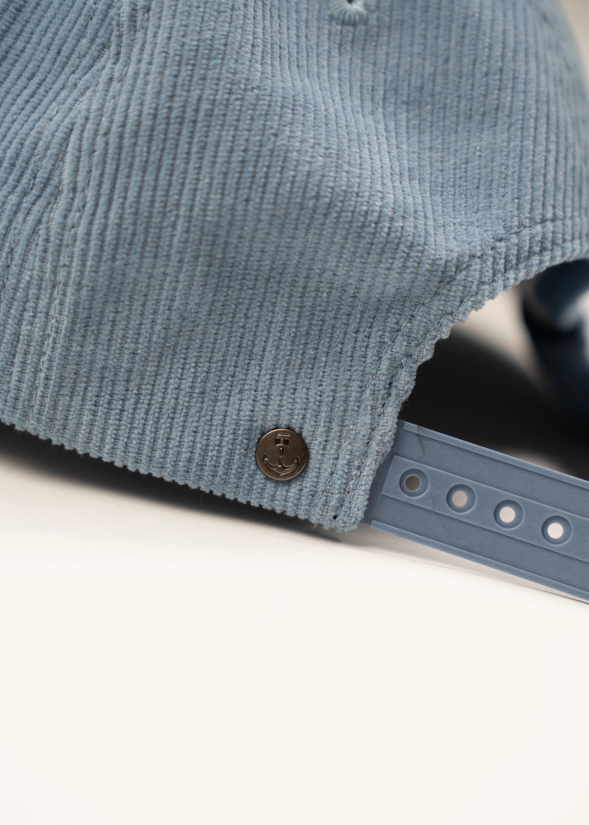Close-up of a blue corduroy cap with an anchor button and adjustable strap on a white background.
