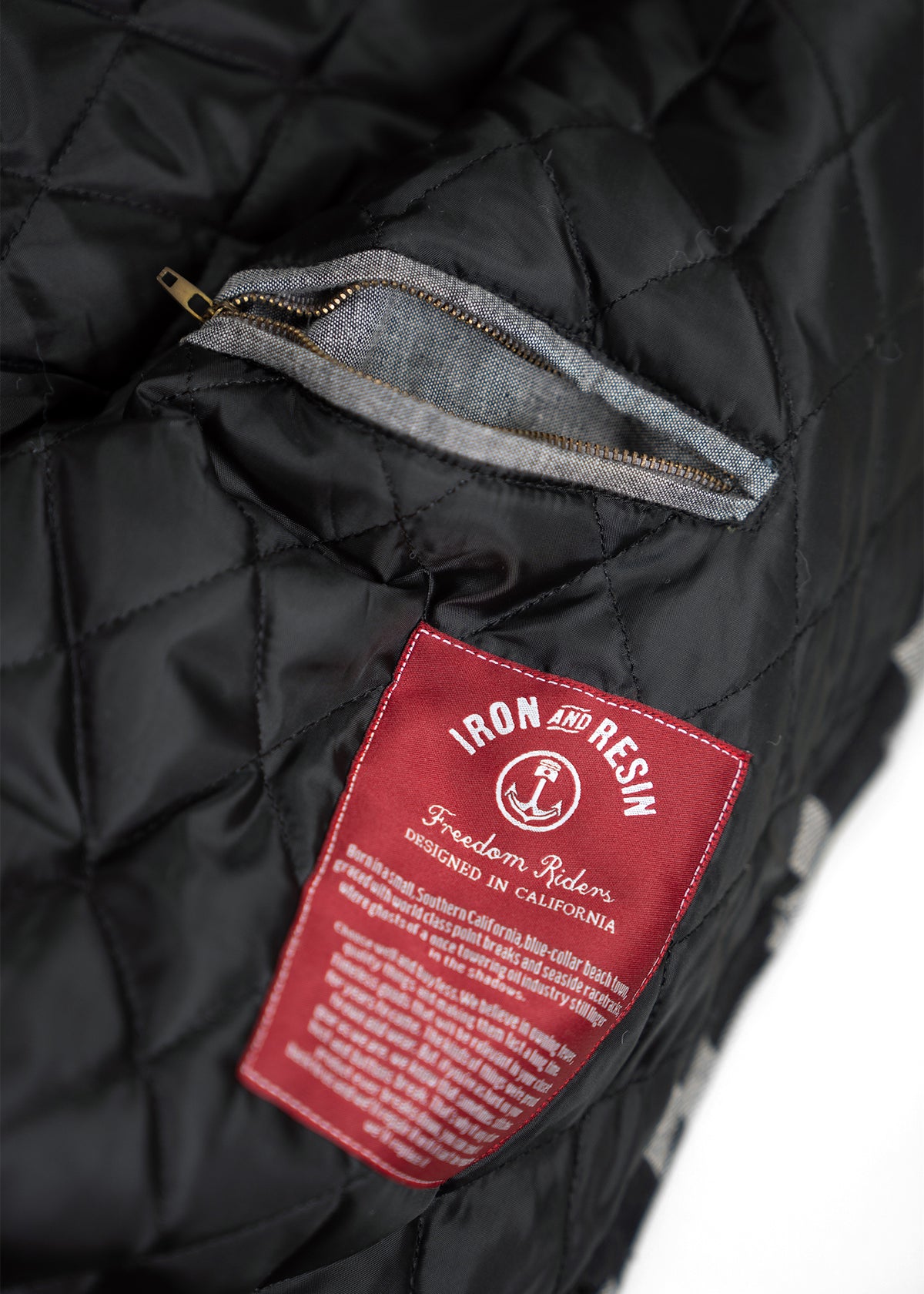 Quilted black jacket with a red "Iron and Resin" label and open zip pocket, showcasing California design craftsmanship.