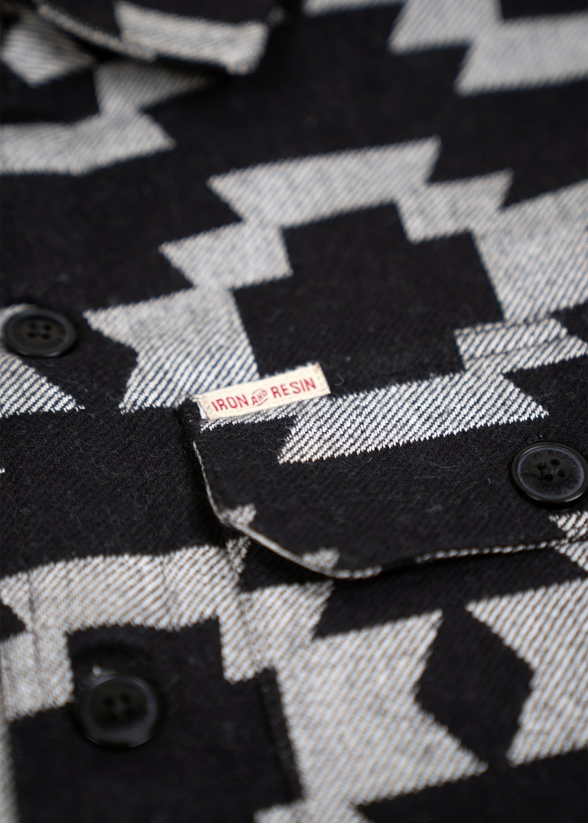 Close-up of a black and white geometric patterned shirt with black buttons and an Iron and Resin label on the pocket flap.