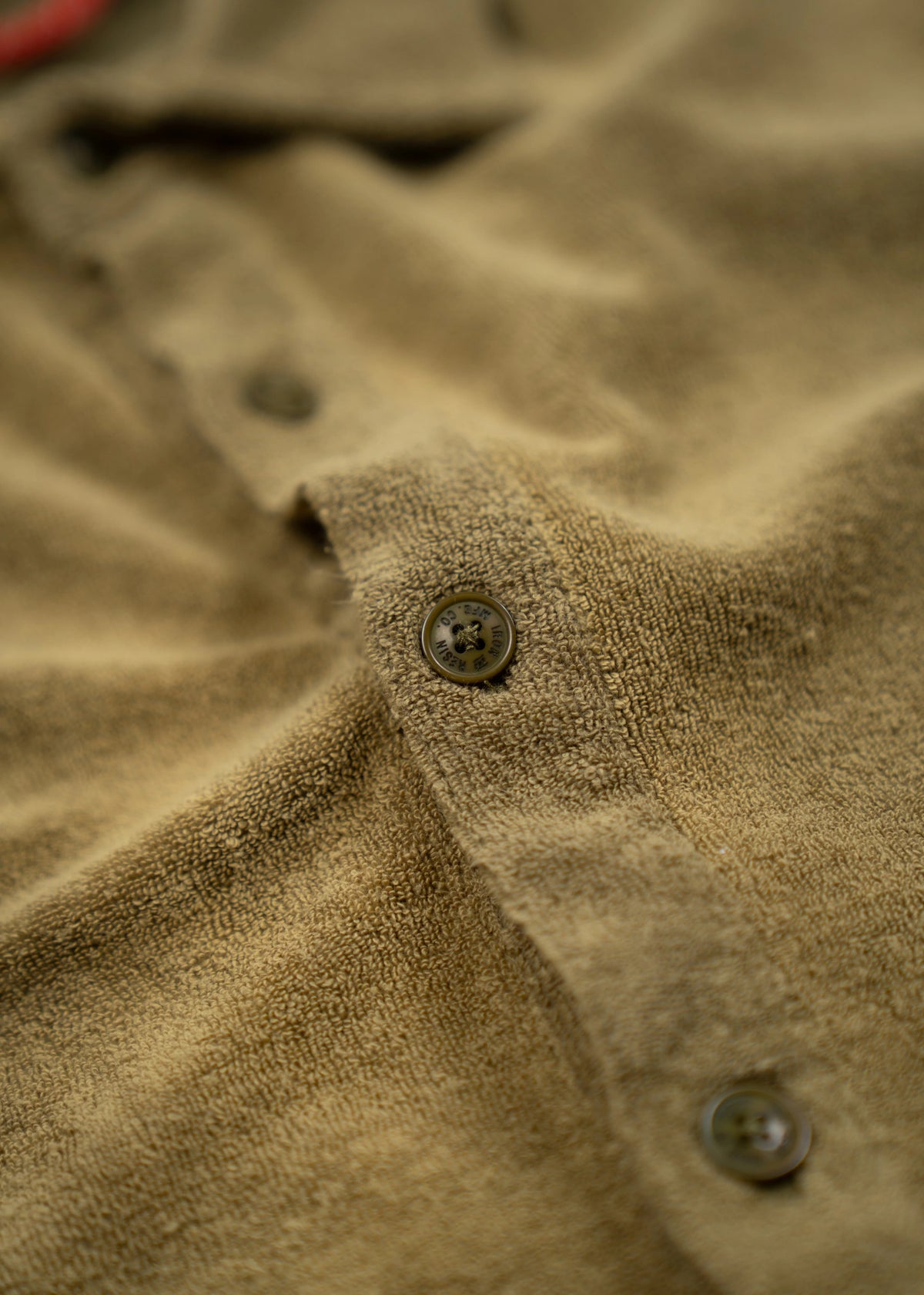 Close-up of a brown textured fabric shirt with visible buttons, highlighting the material's softness and detailed stitching.