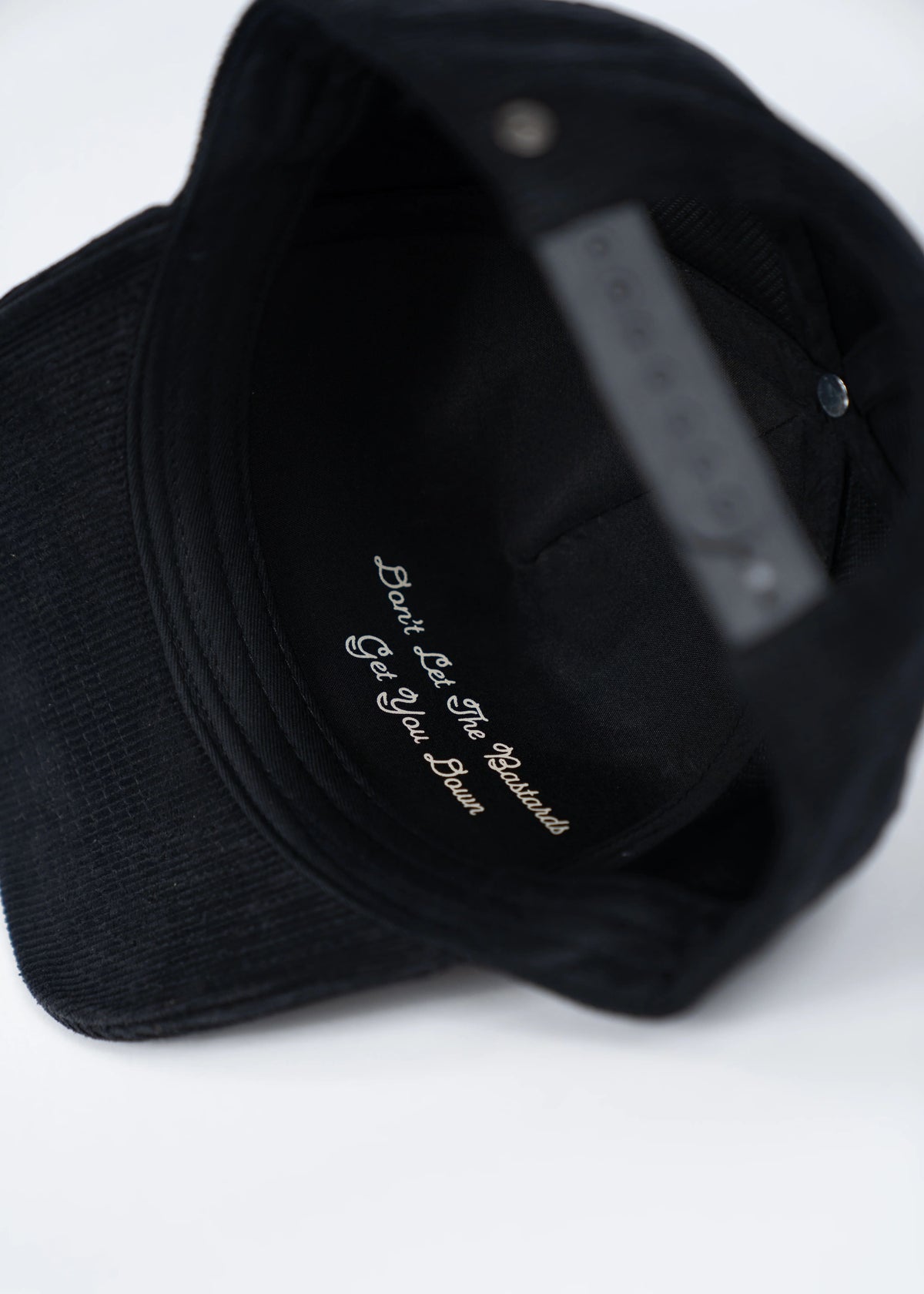 Black cap with inner text: "Don't Let The Bastards Get You Down" in white script. Simple and motivational design.