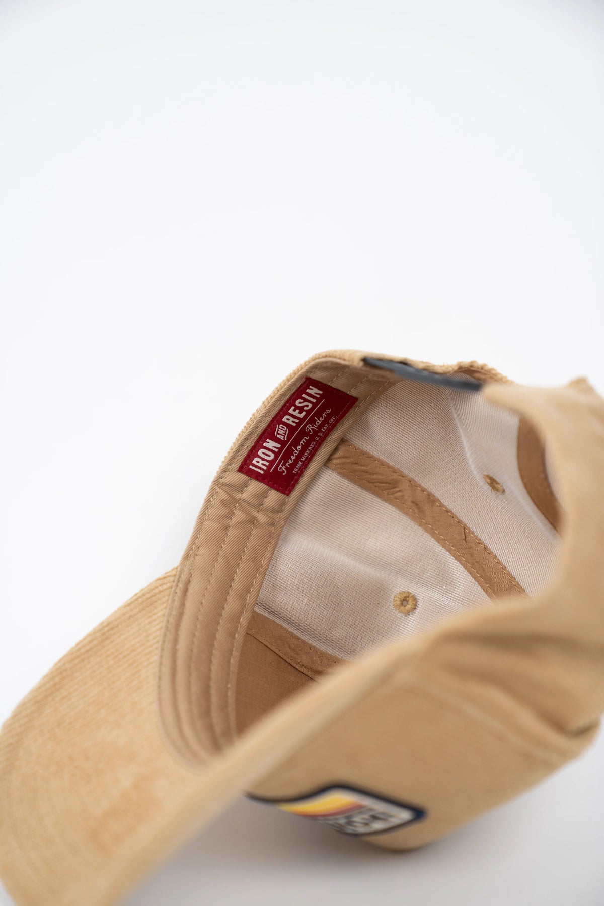 Tan cap interior with red "Iron and Resin" label, white stitching, and a patch on the brim, viewed from above on white background.