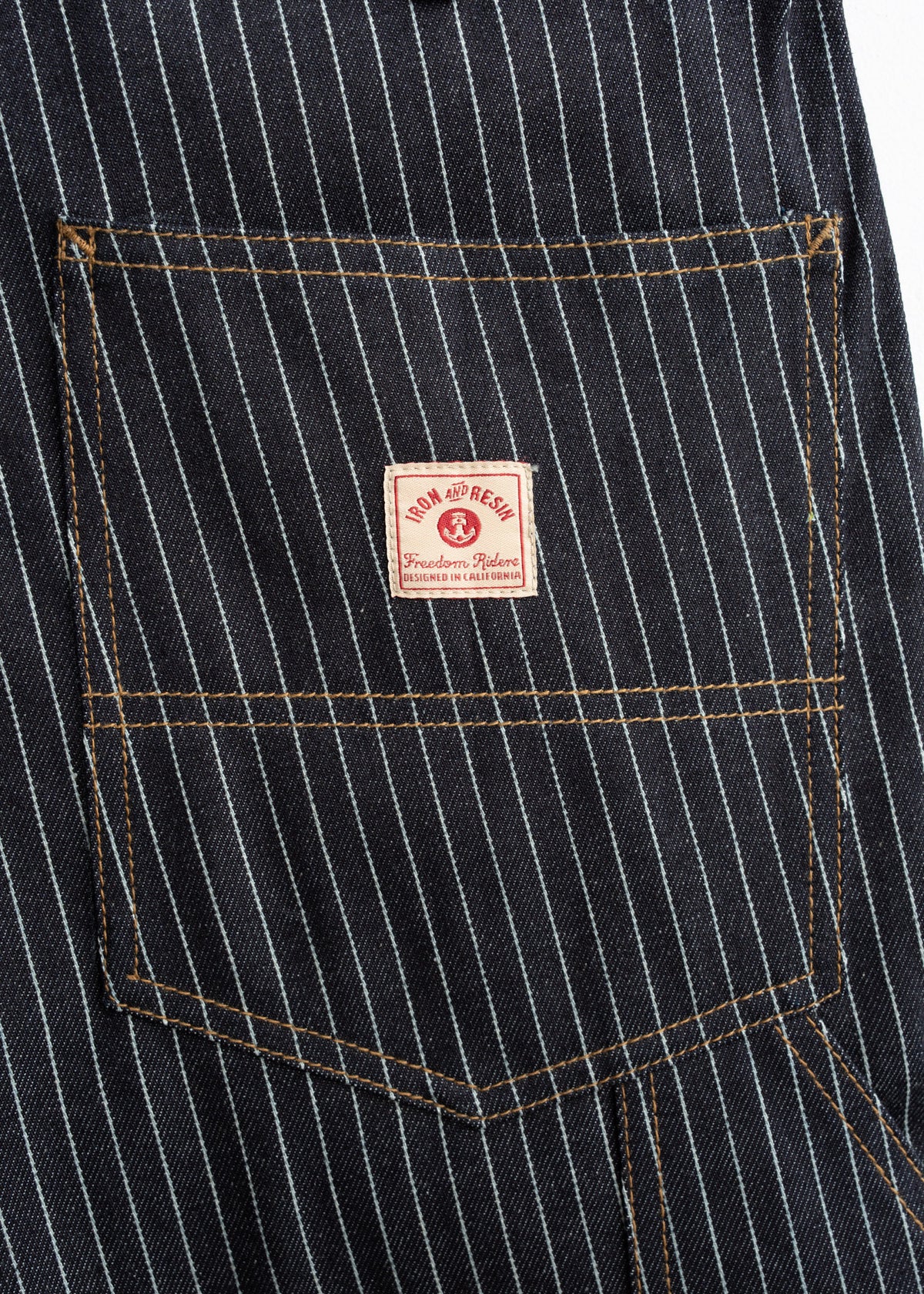Close-up of a pinstriped denim pocket with a red "Iron and Resin" label, showcasing detailed stitching and classic design.