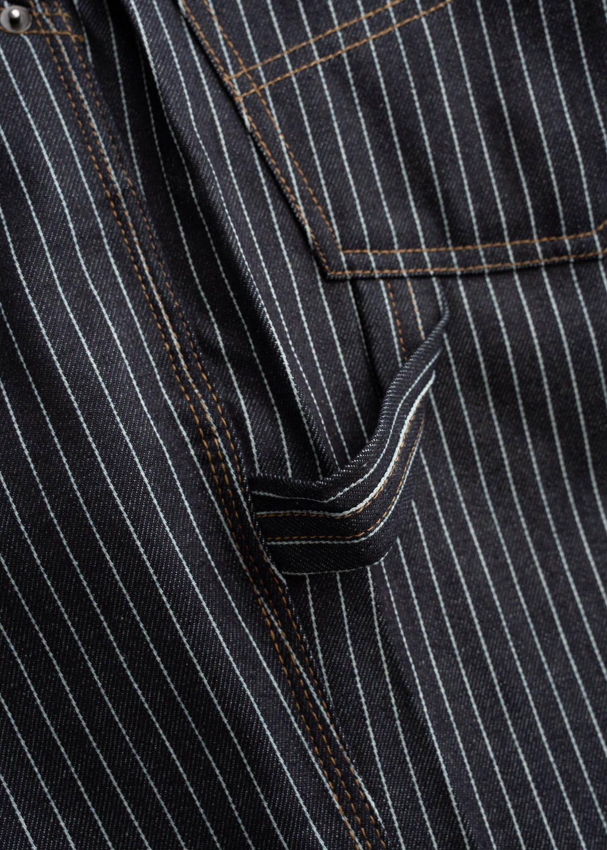 Close-up of a black pinstripe fabric with brown stitching, showing a pocket and belt loop detail.