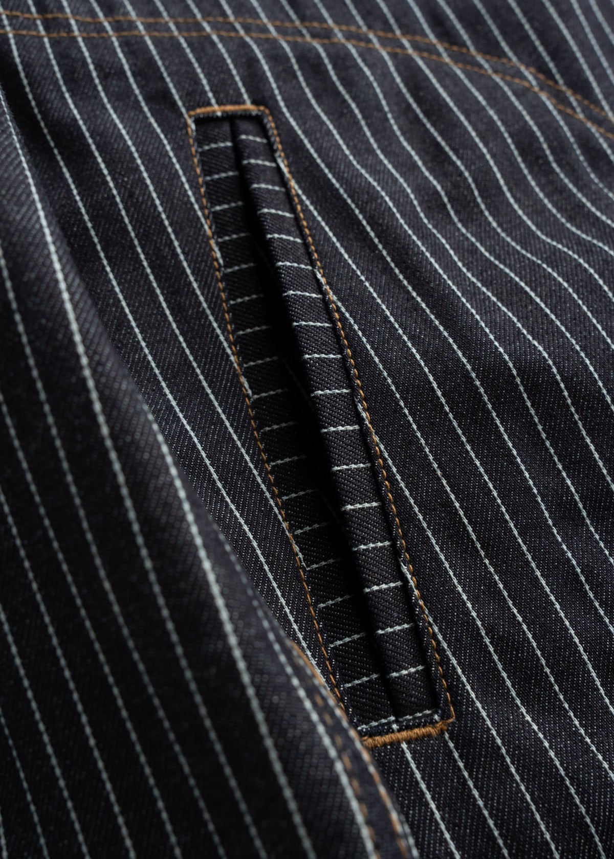 Close-up of a pinstripe fabric with a neatly stitched pocket, showcasing detailed craftsmanship and contrasting thread.