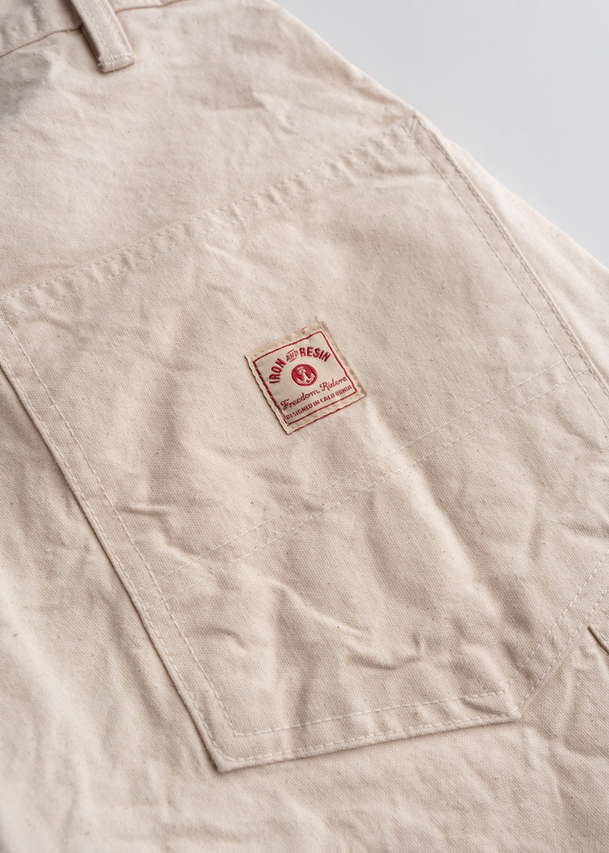 Close-up of beige fabric with a pocket featuring a red "Iron and Resin" label, highlighting craftsmanship and style.
