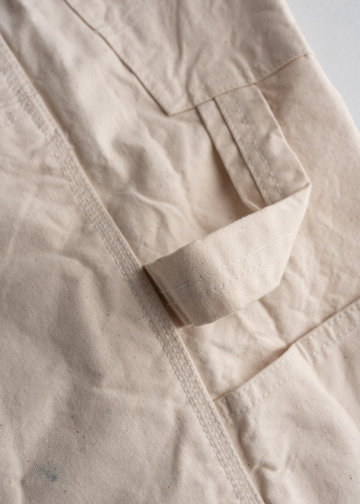 Close-up of beige canvas fabric with a stitched loop and seam detail, showcasing texture and craftsmanship.
