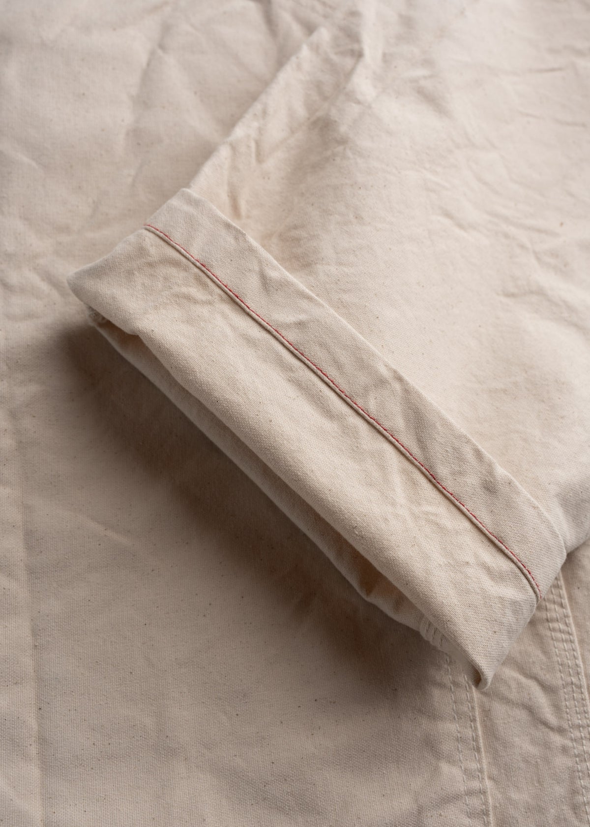 Close-up of a beige fabric with a folded hem, featuring red stitching detail on a textured surface.
