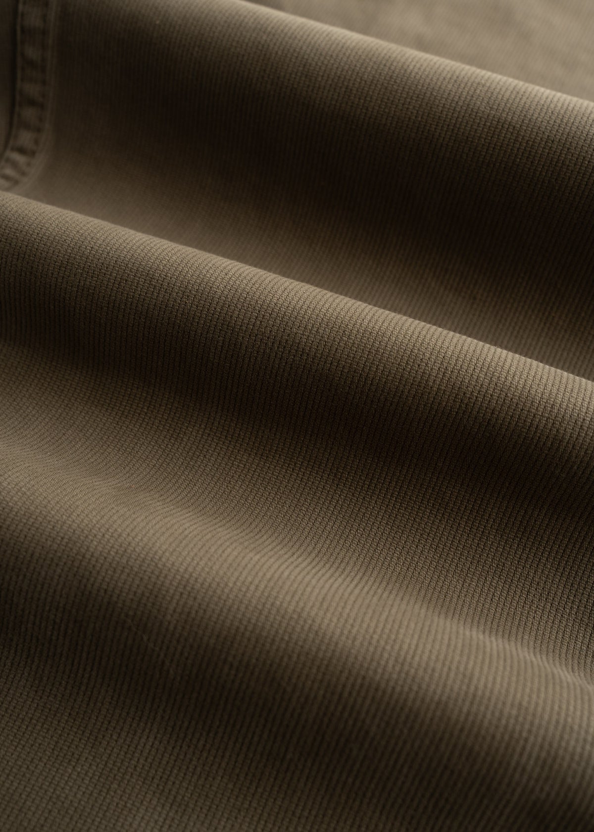 Close-up of brown corduroy fabric with soft, parallel ridges creating a textured, wavy pattern in gentle lighting.