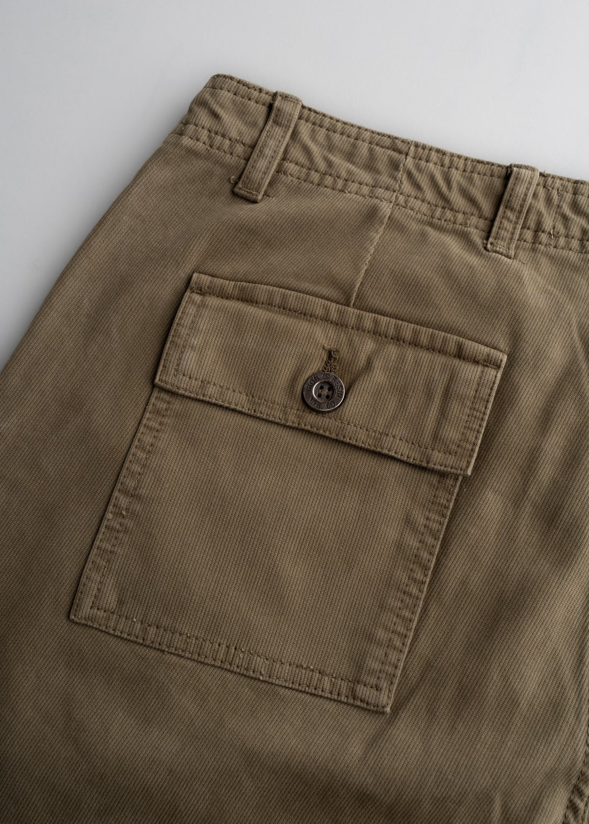 Close-up of khaki pants showing a buttoned back pocket and belt loops, highlighting the fabric texture and stitching details.