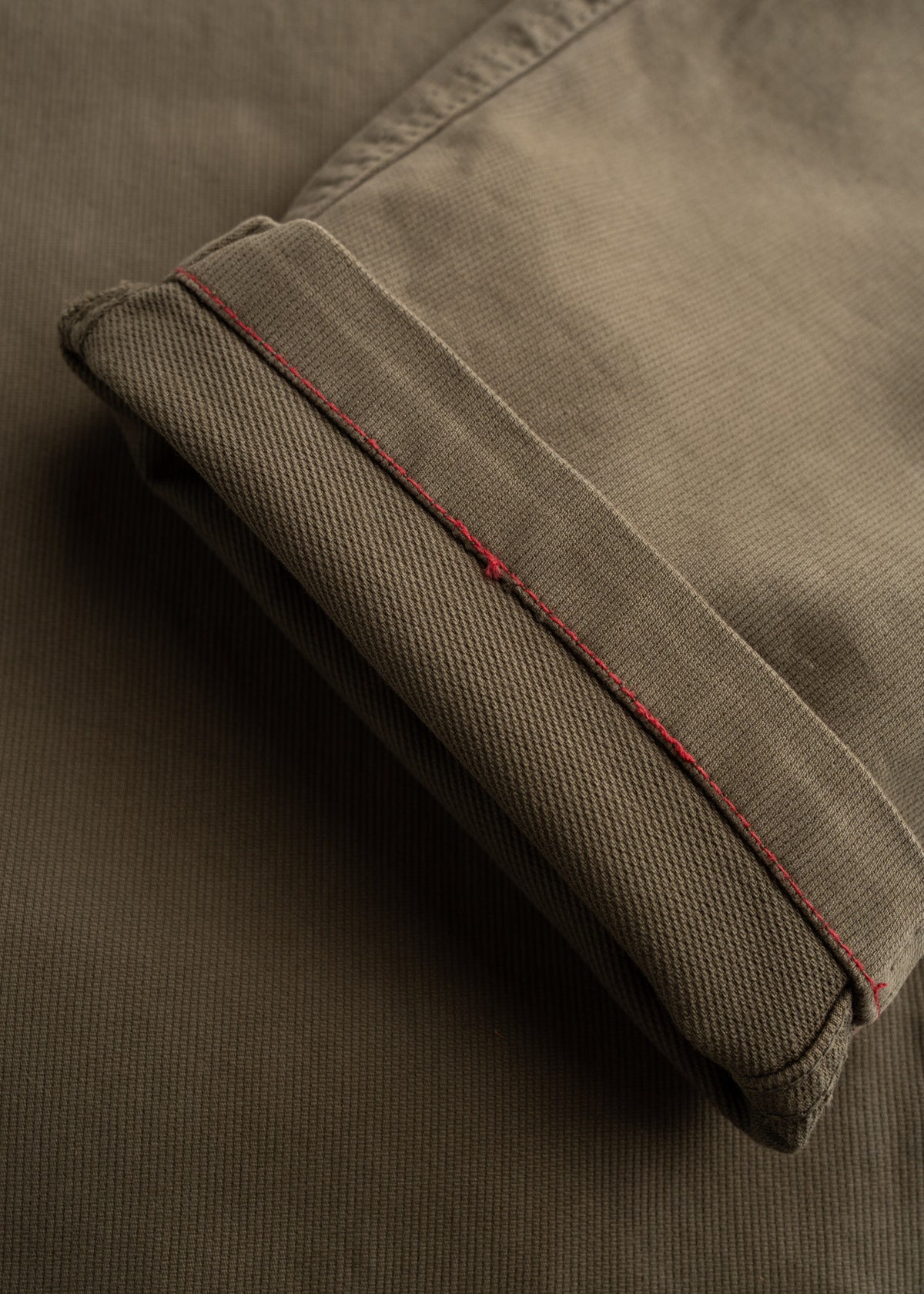 Close-up of brown fabric with a folded edge, highlighted by red stitching, showing texture and detail.