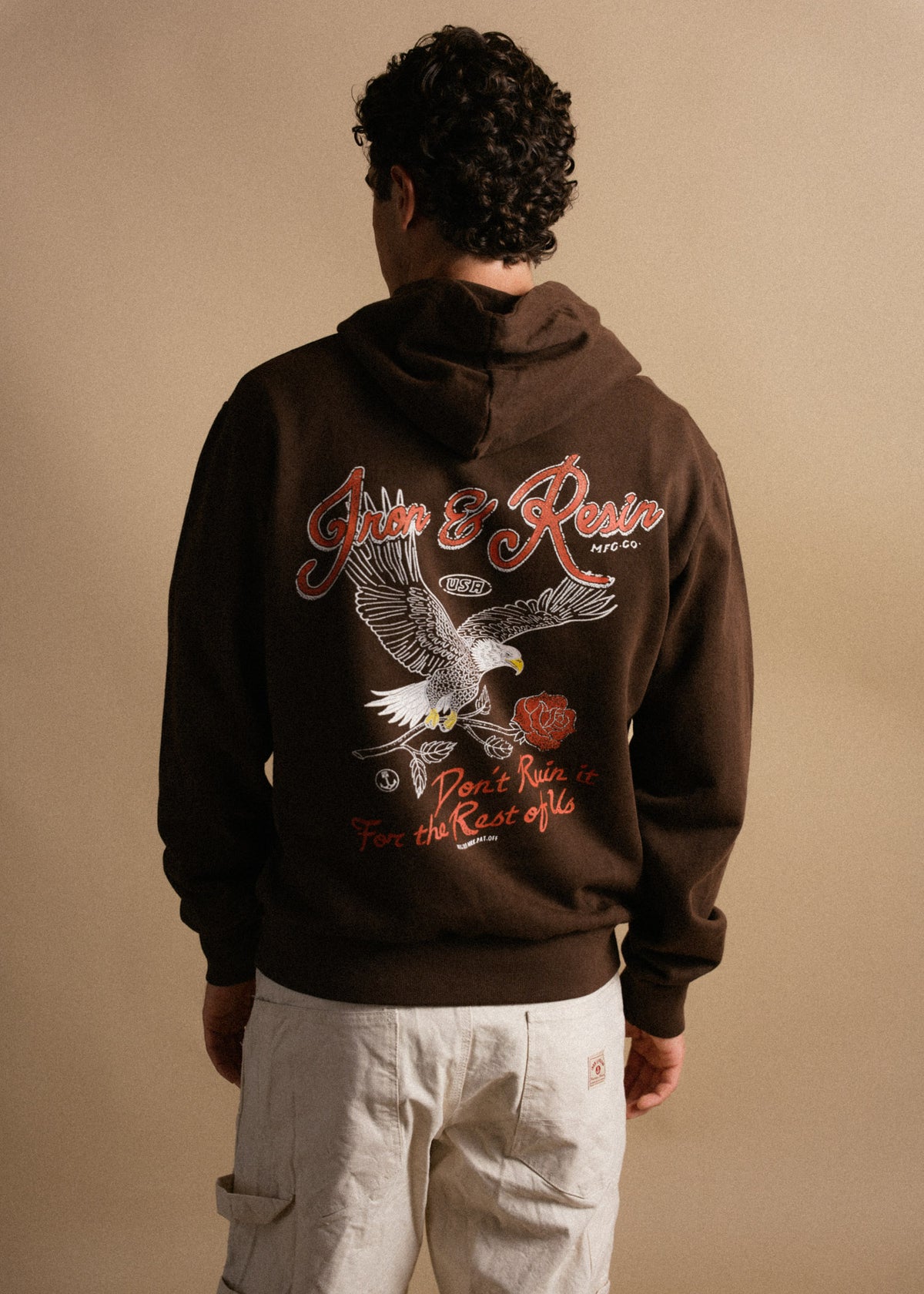 Man in brown hoodie with eagle and rose design, text reads "Iron & Resin, Don't Ruin it for the Rest of Us," beige pants.