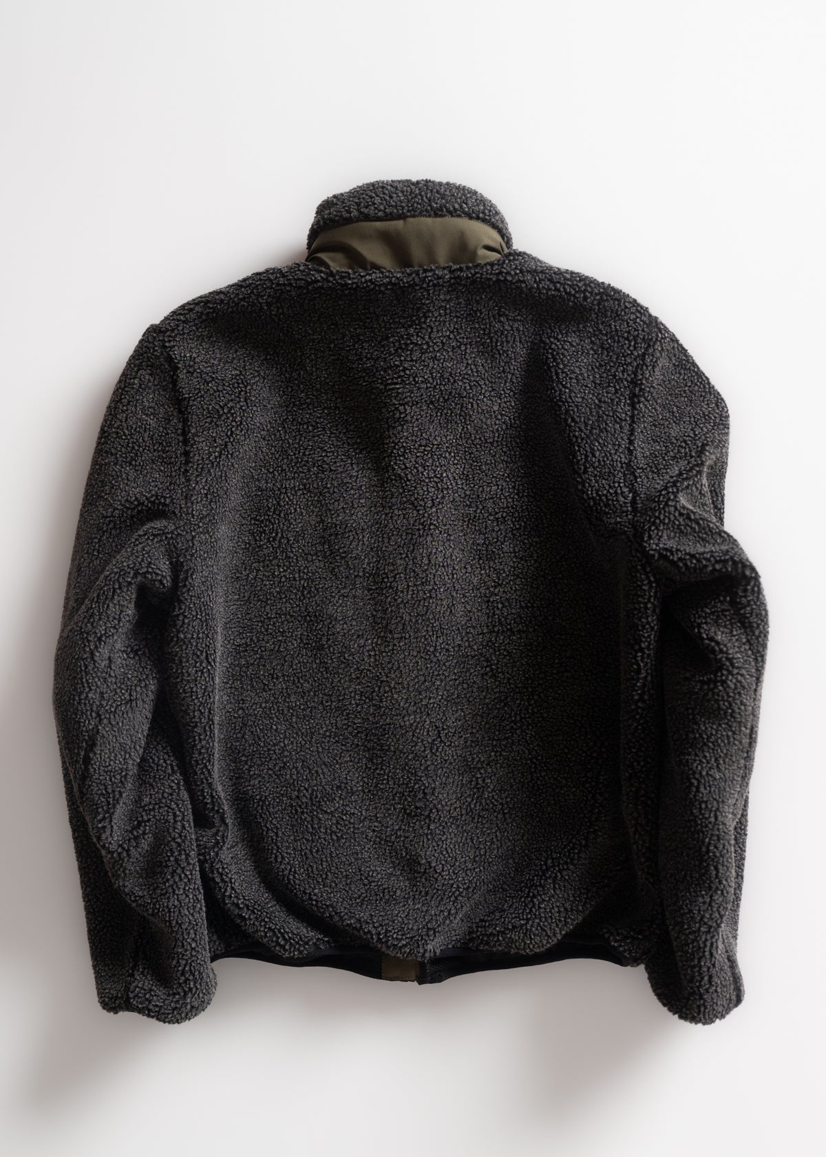 A cozy, dark gray fleece jacket with a high collar is displayed against a plain white background, highlighting its texture.