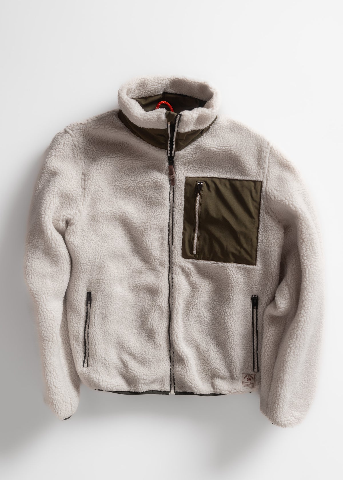 Cream fleece jacket with olive chest pocket and black zippers, laid flat on a white background.
