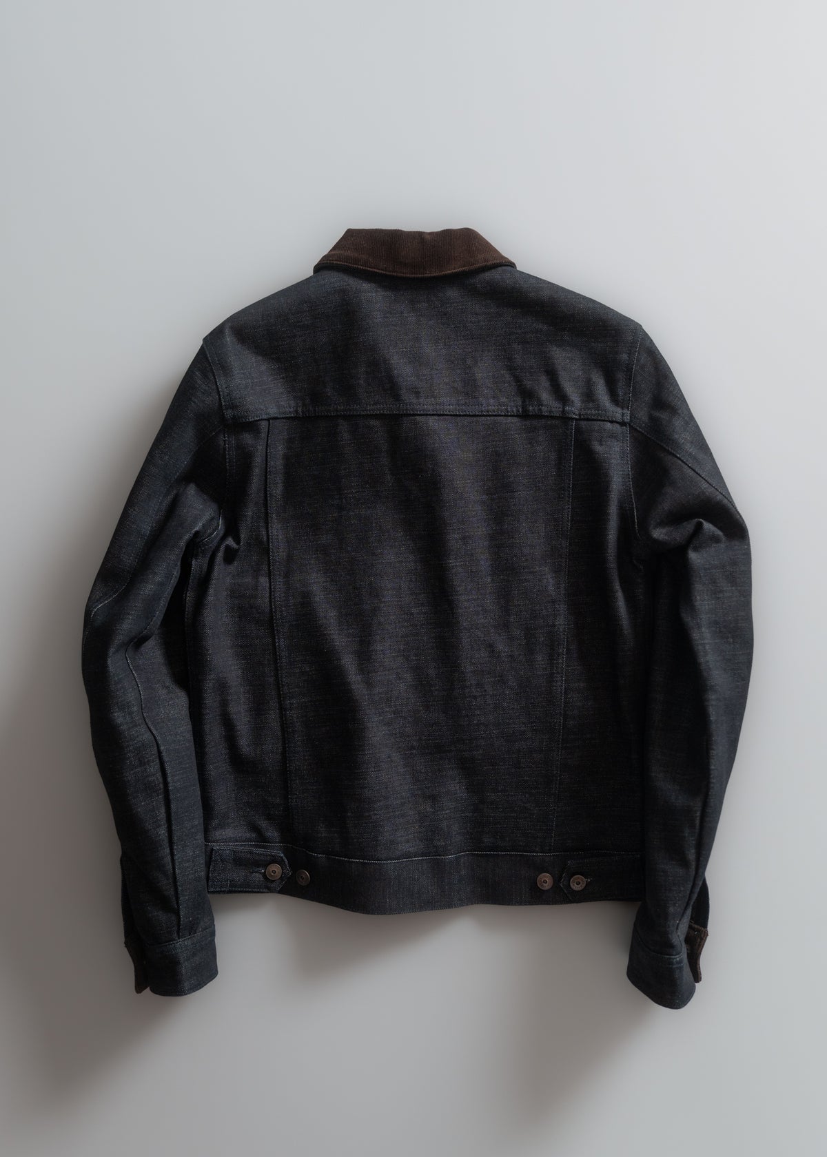 Dark denim jacket with a brown collar, displayed on a light background, showcasing its back design and button details.