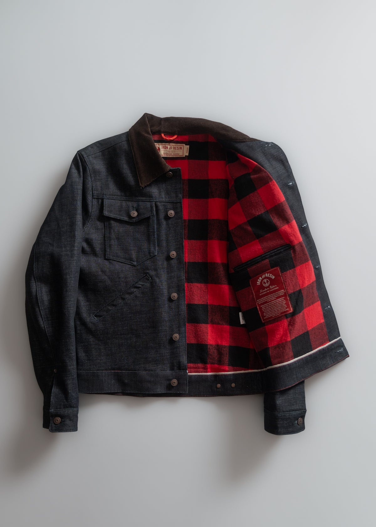 Denim jacket with red plaid lining displayed open on a white background, showcasing its stylish design and contrasting interior.