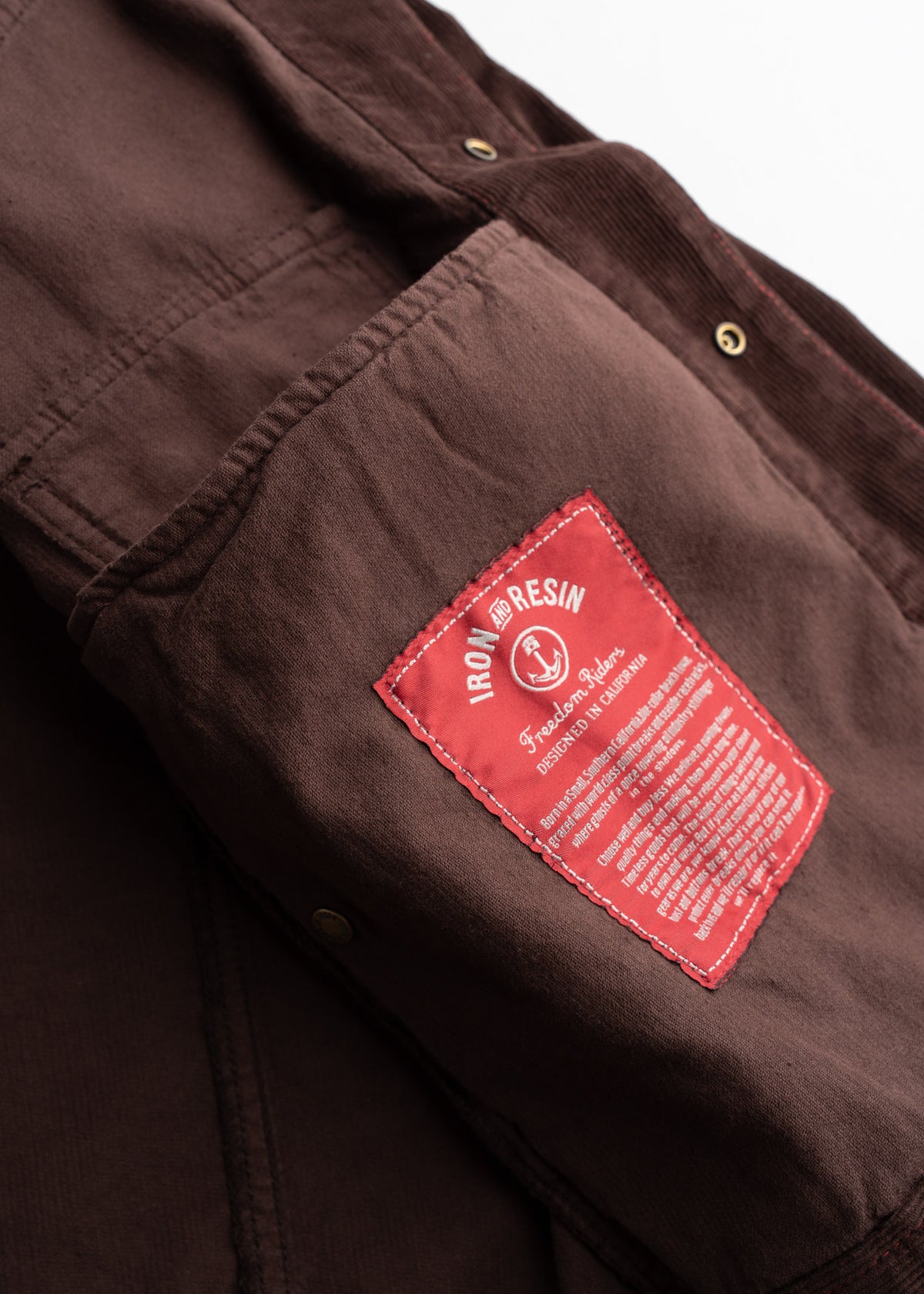 Close-up of a brown jacket with a red Iron and Resin label, featuring detailed stitching and metal buttons, showcasing craftsmanship.
