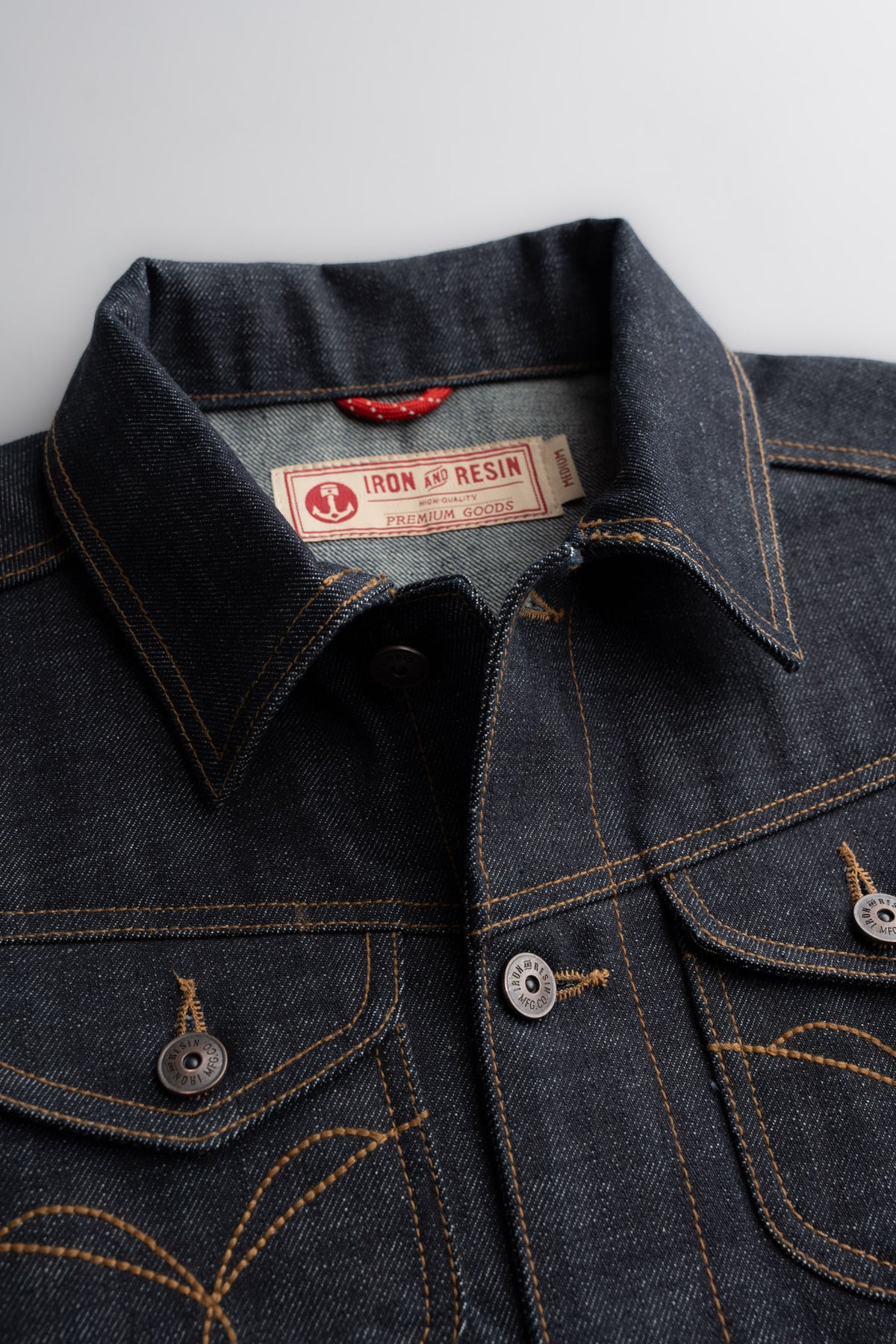 Denim jacket close-up with Iron and Resin label, showcasing detailed stitching and metal buttons on a textured fabric surface.