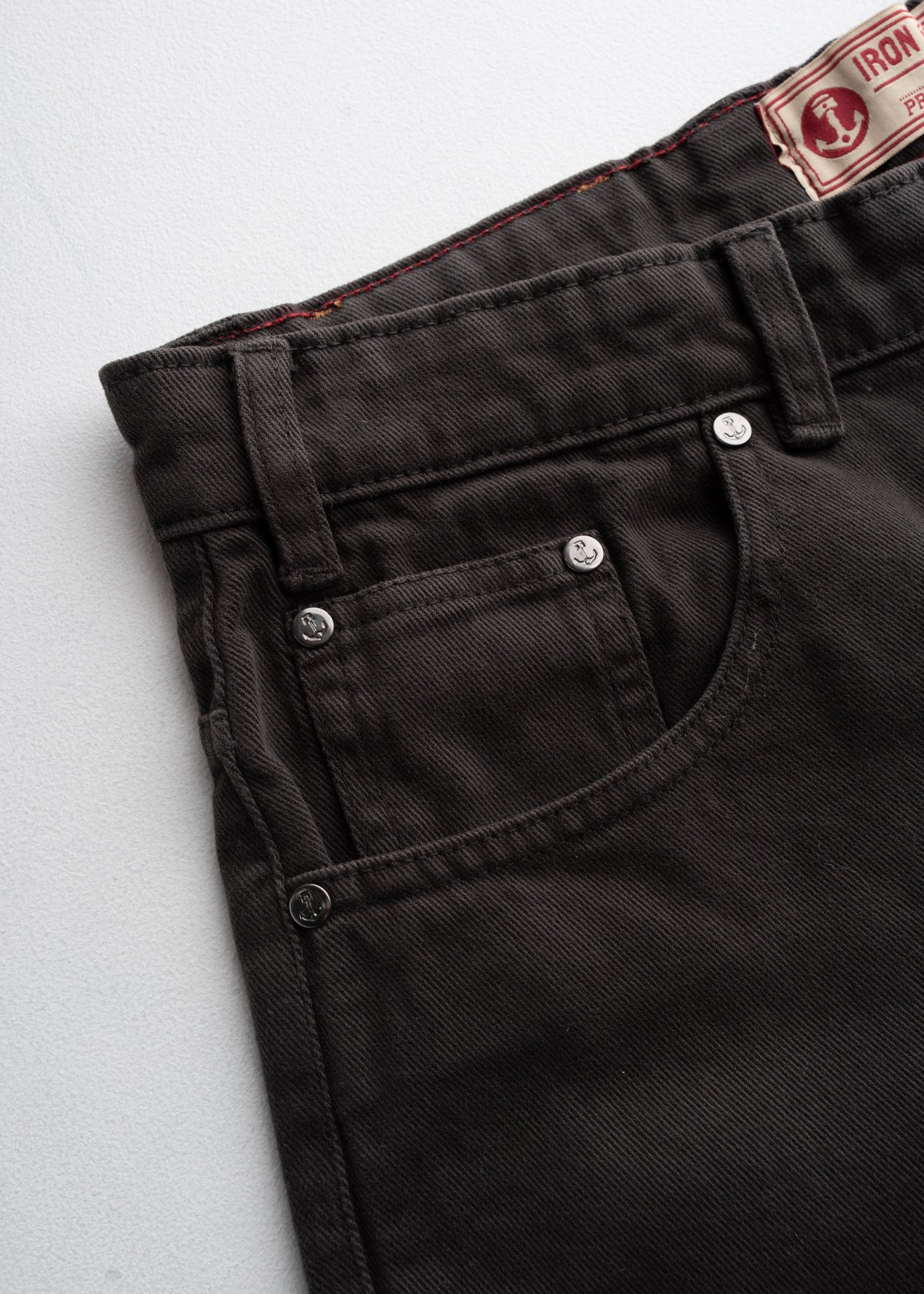 Close-up of black denim jeans with silver rivets and a visible label on a white background.