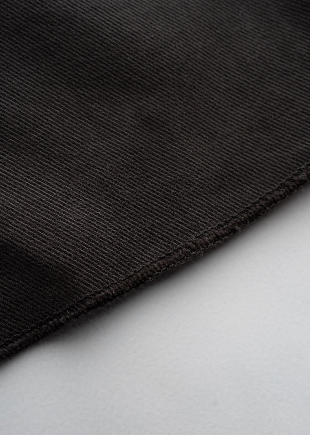Close-up of dark brown corduroy fabric with visible texture and stitched edge on a light gray background.