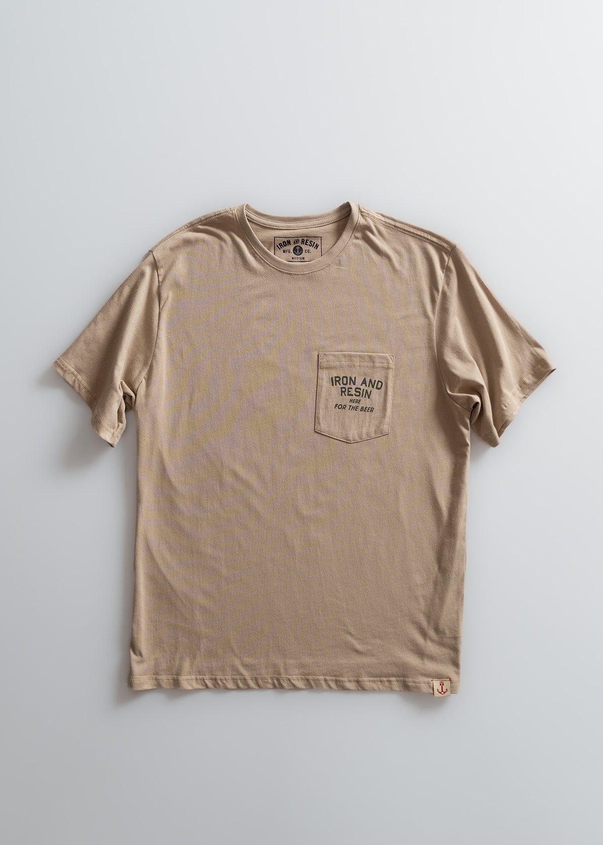Beige t-shirt with "Iron and Resin" logo on chest pocket, laid flat on a light background, showcasing casual style.