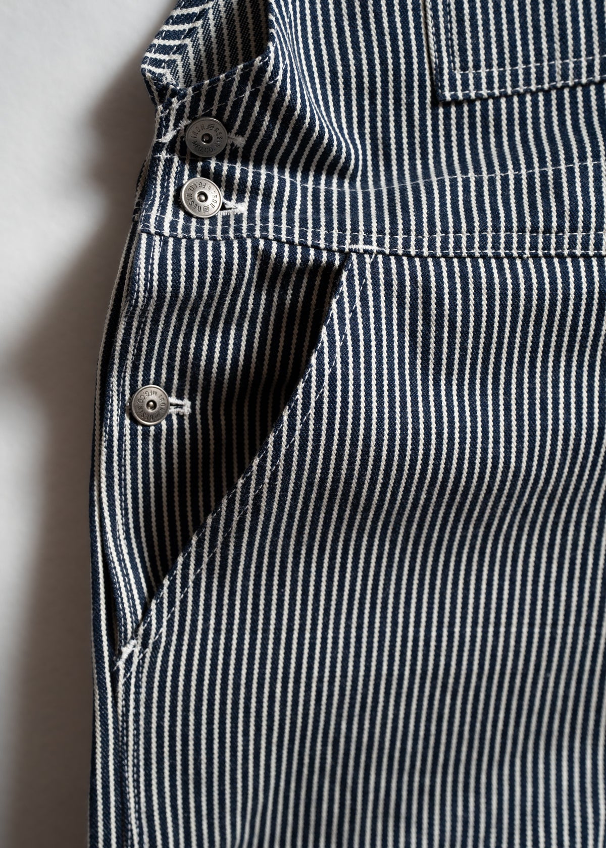 Close-up of blue and white striped fabric with metal buttons, showcasing detailed stitching and texture in natural light.