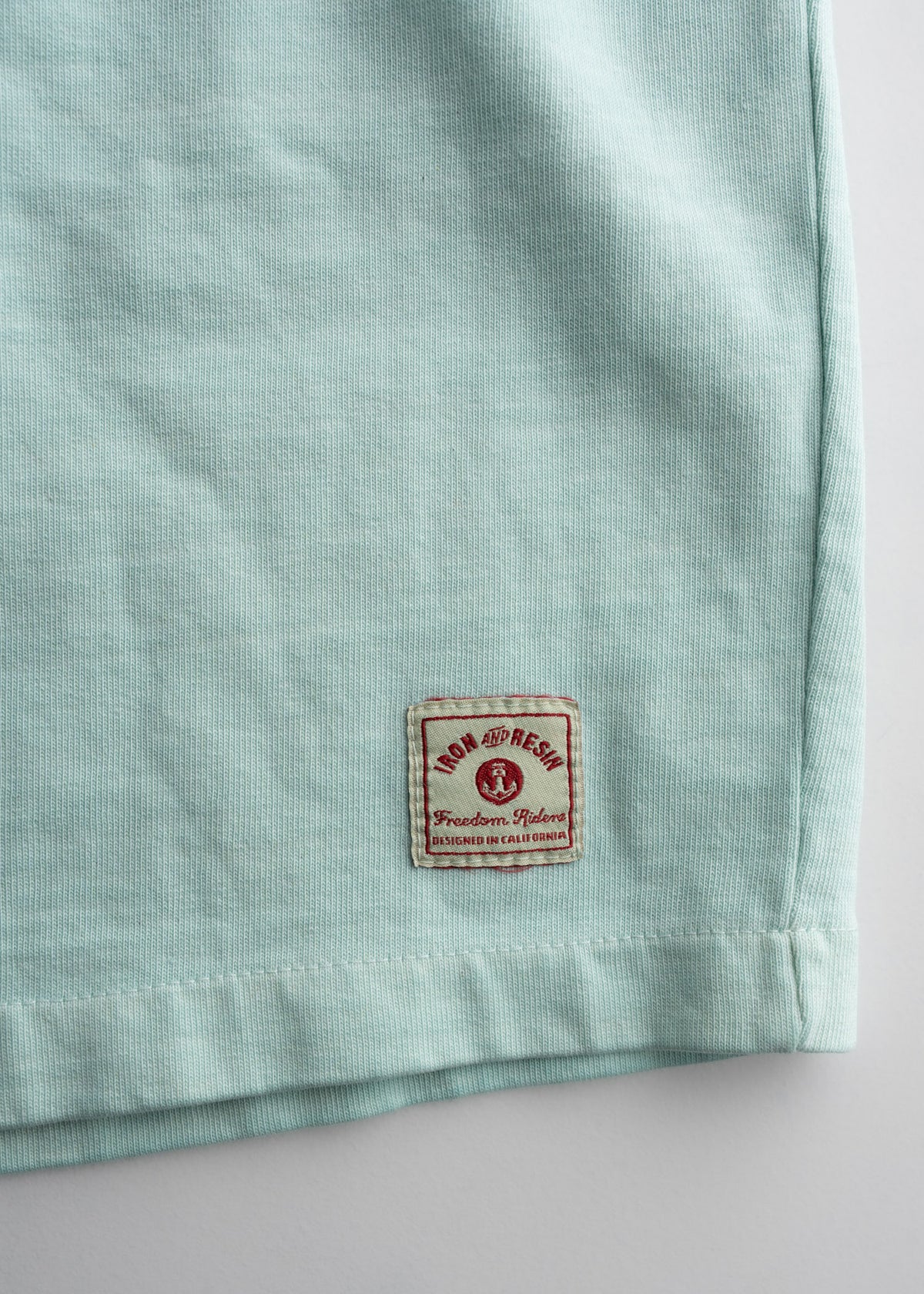 Men’s 9.5 oz jersey cotton shorts in light Blue, close-up shot detailing fabric quality and custom logo tag