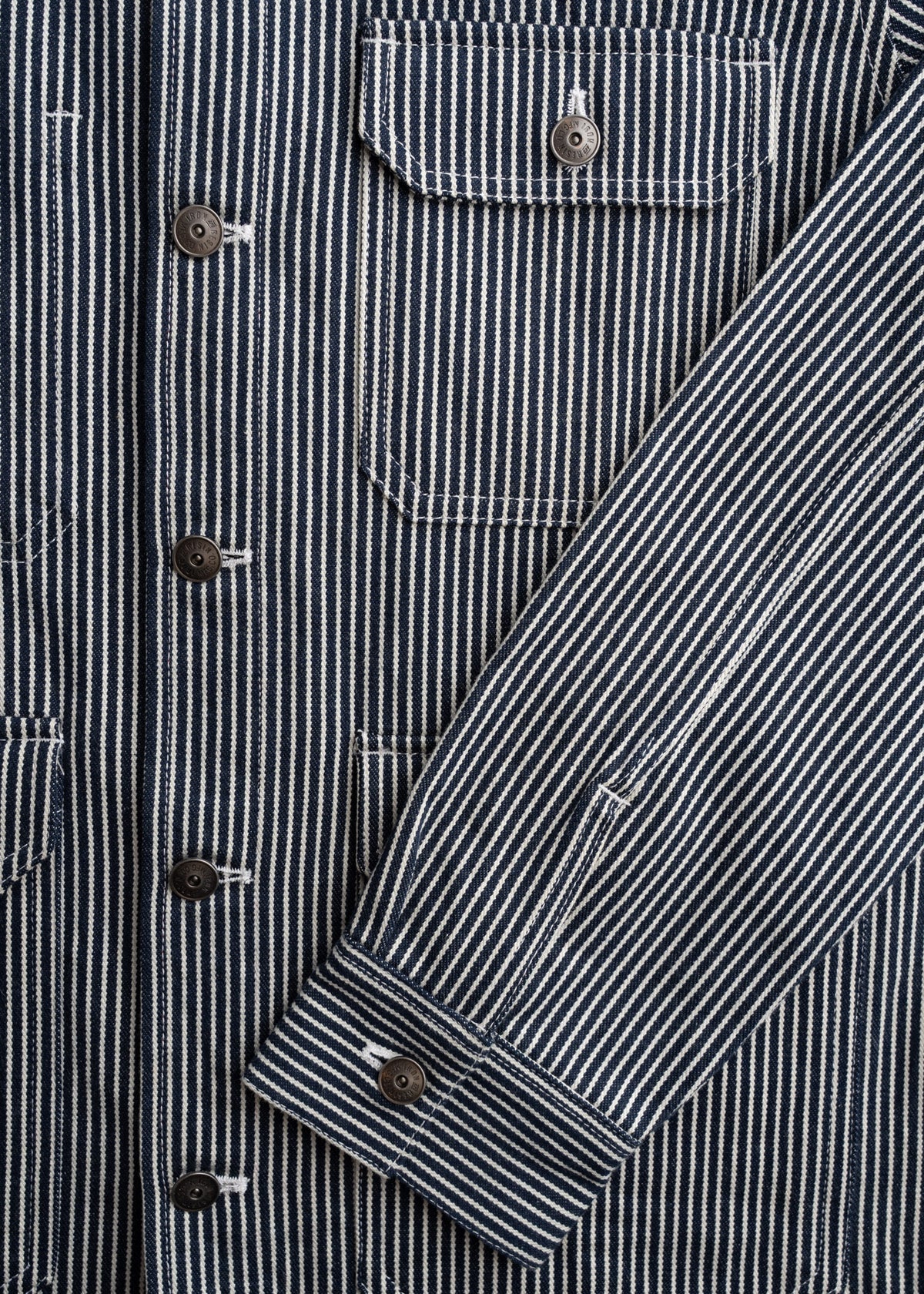 Close-up of a blue and white striped shirt with buttoned pockets and sleeve, showcasing detailed stitching and fabric texture.