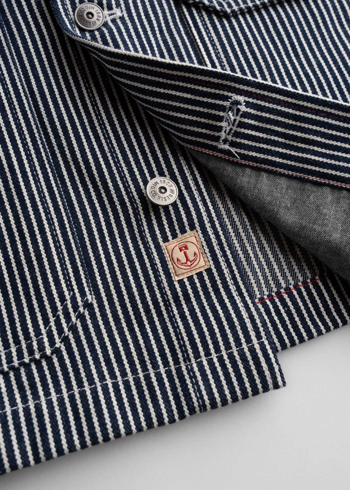 Close-up of a blue and white striped fabric with buttons and a red anchor logo, showcasing detailed stitching and texture.
