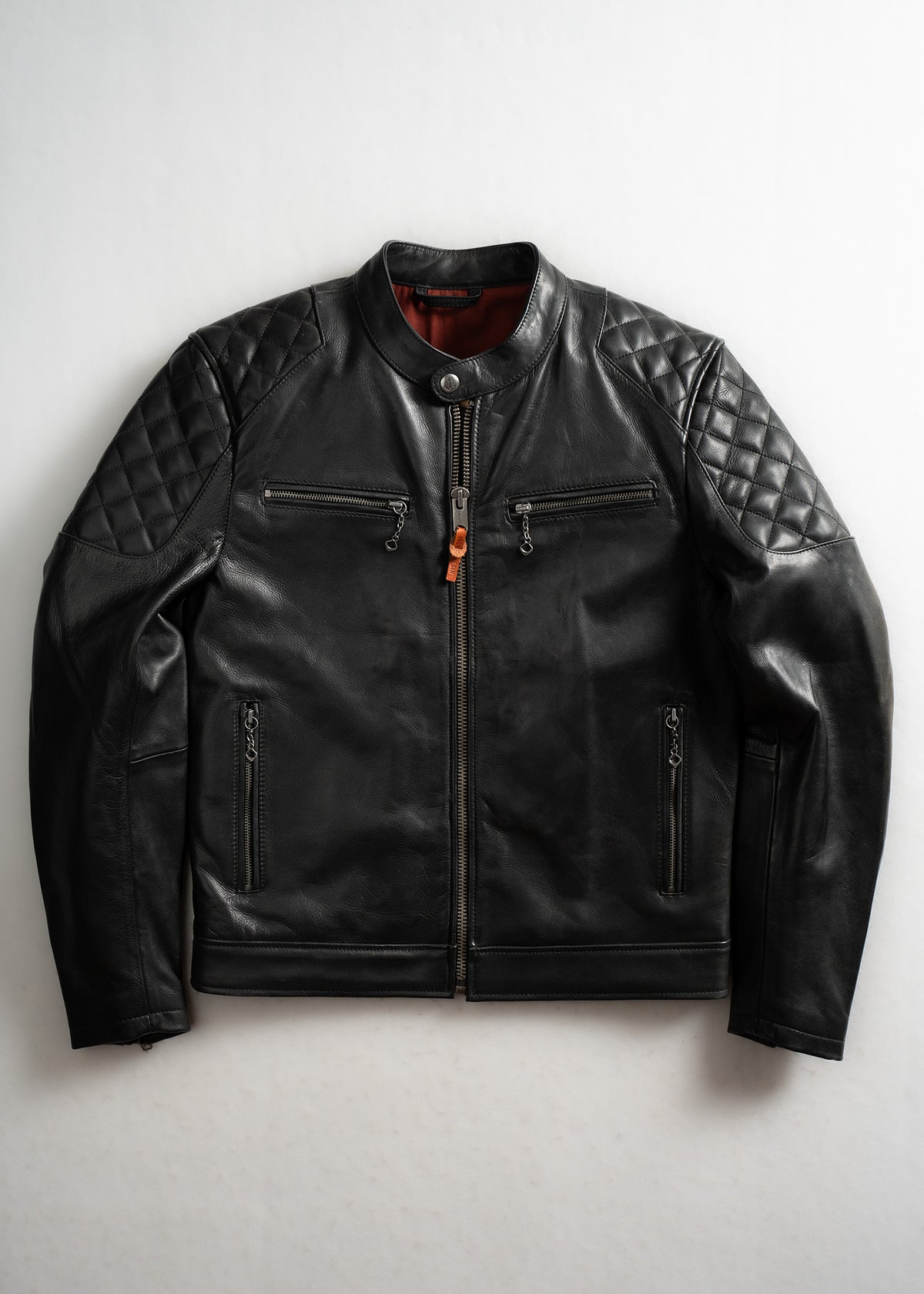 Black leather jacket with quilted shoulders, zip pockets, and orange lining, laid flat on a white background.