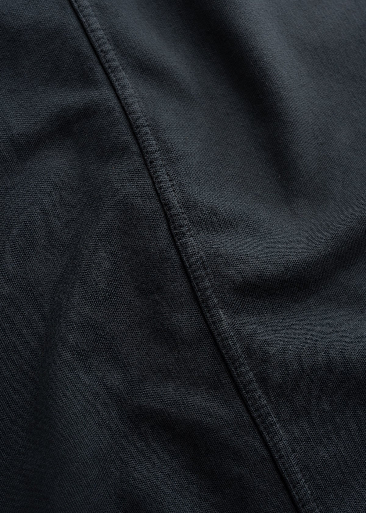 Close-up of a dark fabric with a visible seam running diagonally, highlighting texture and stitching details.
