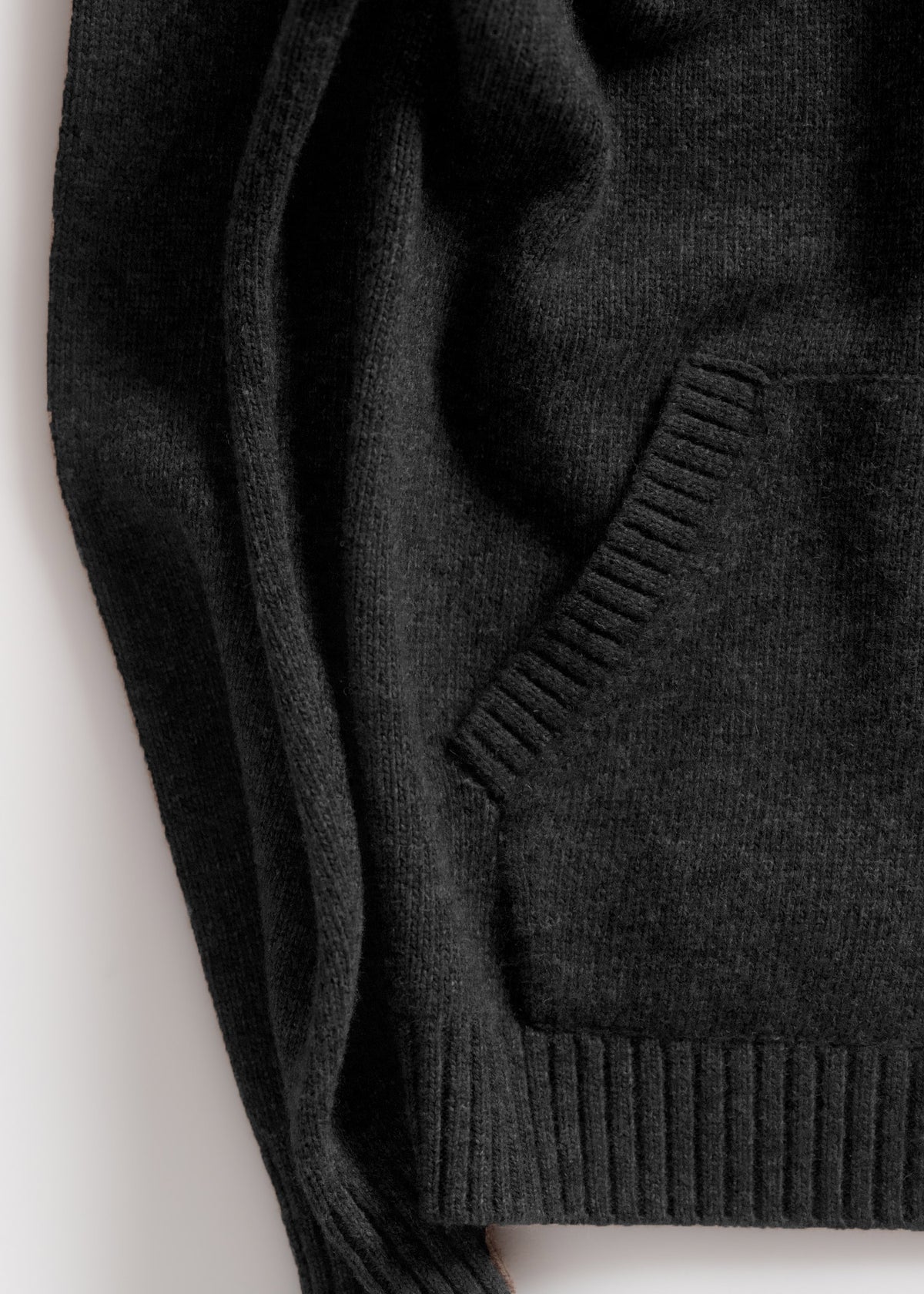 Close-up of a dark gray knit sweater with a ribbed pocket and hem, showcasing its texture and cozy design.