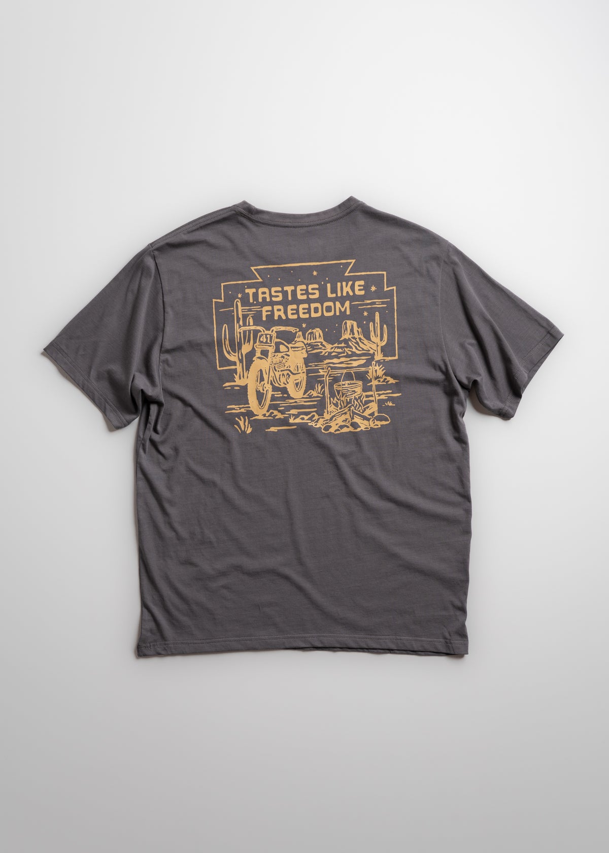 Gray T-shirt with "Tastes Like Freedom" and desert scene printed in yellow on the back, featuring cacti and a motorcycle.