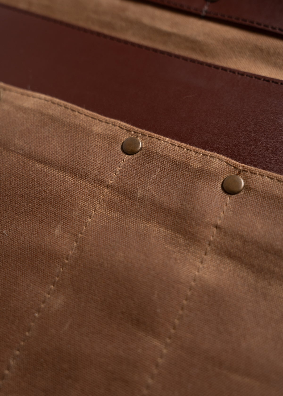 Close-up of brown canvas fabric with two metal rivets, showing texture and stitching details.