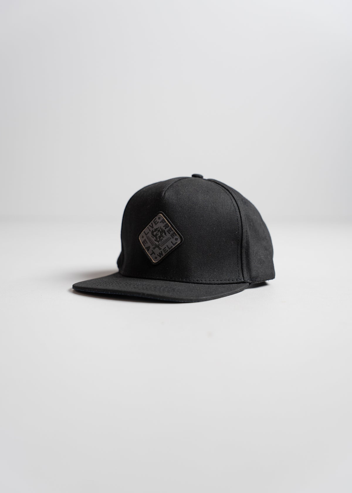 A black snapback cap with a square logo on the front, placed on a plain white background, showcasing its simple, modern design.