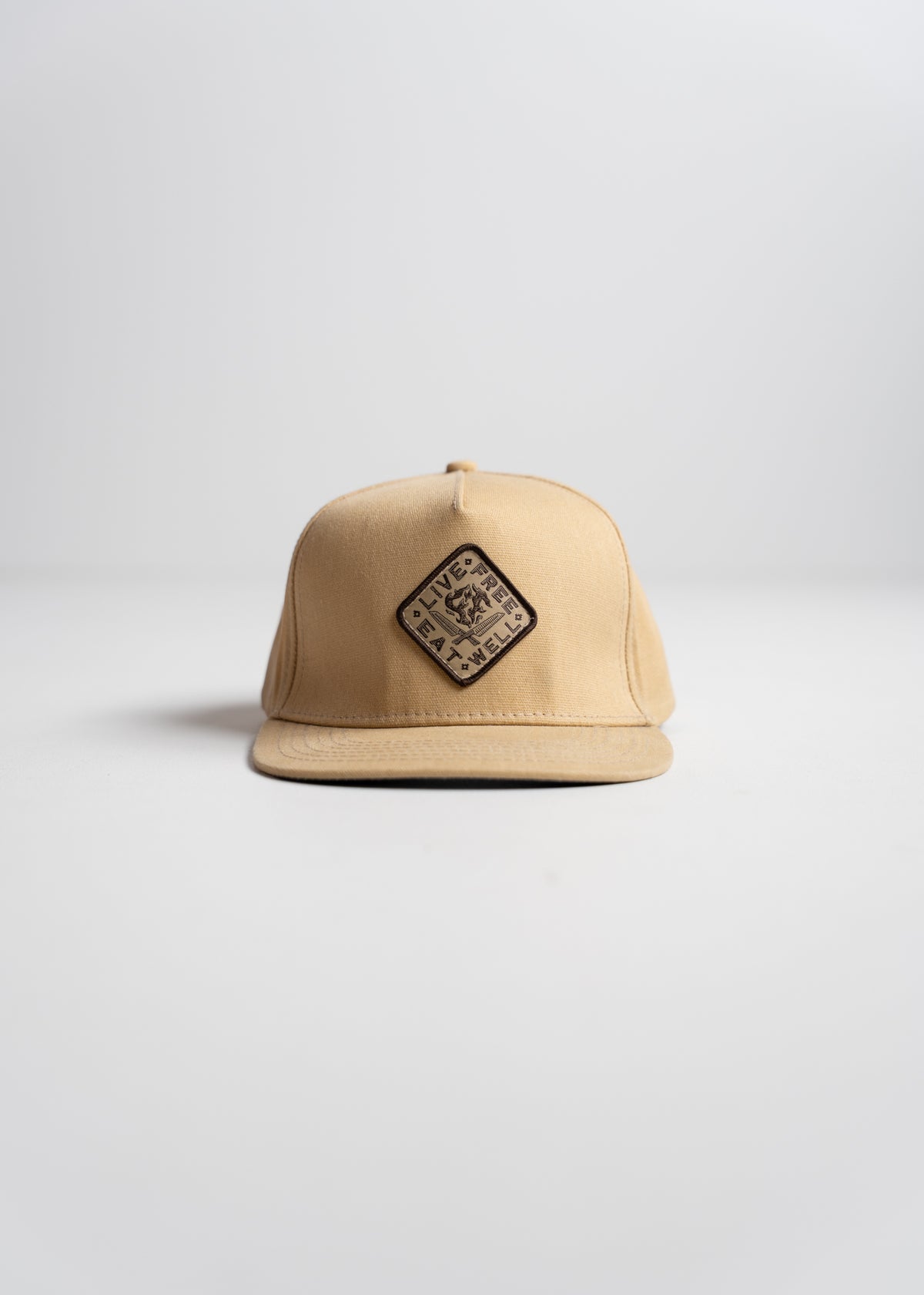 Tan cap with a diamond patch reading "Live Free" on a plain background, emphasizing simplicity and style.