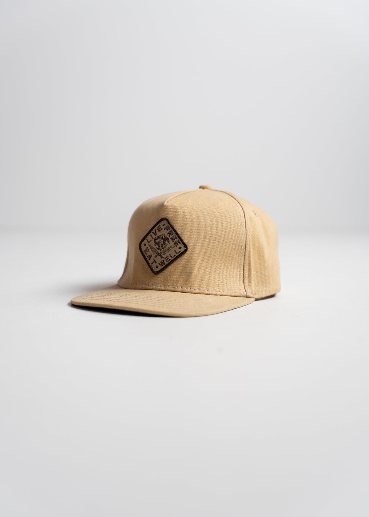 Tan baseball cap with a square patch reading "Live Free" on the front, placed on a plain white background.
